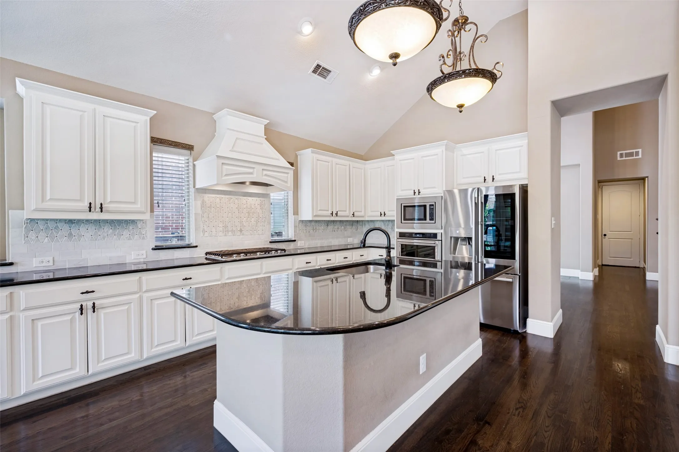 Kitchen featuring a curved central island with a dark countertop, white cabinetry with dark hardware, stainless steel appliances, and a decorative range hood