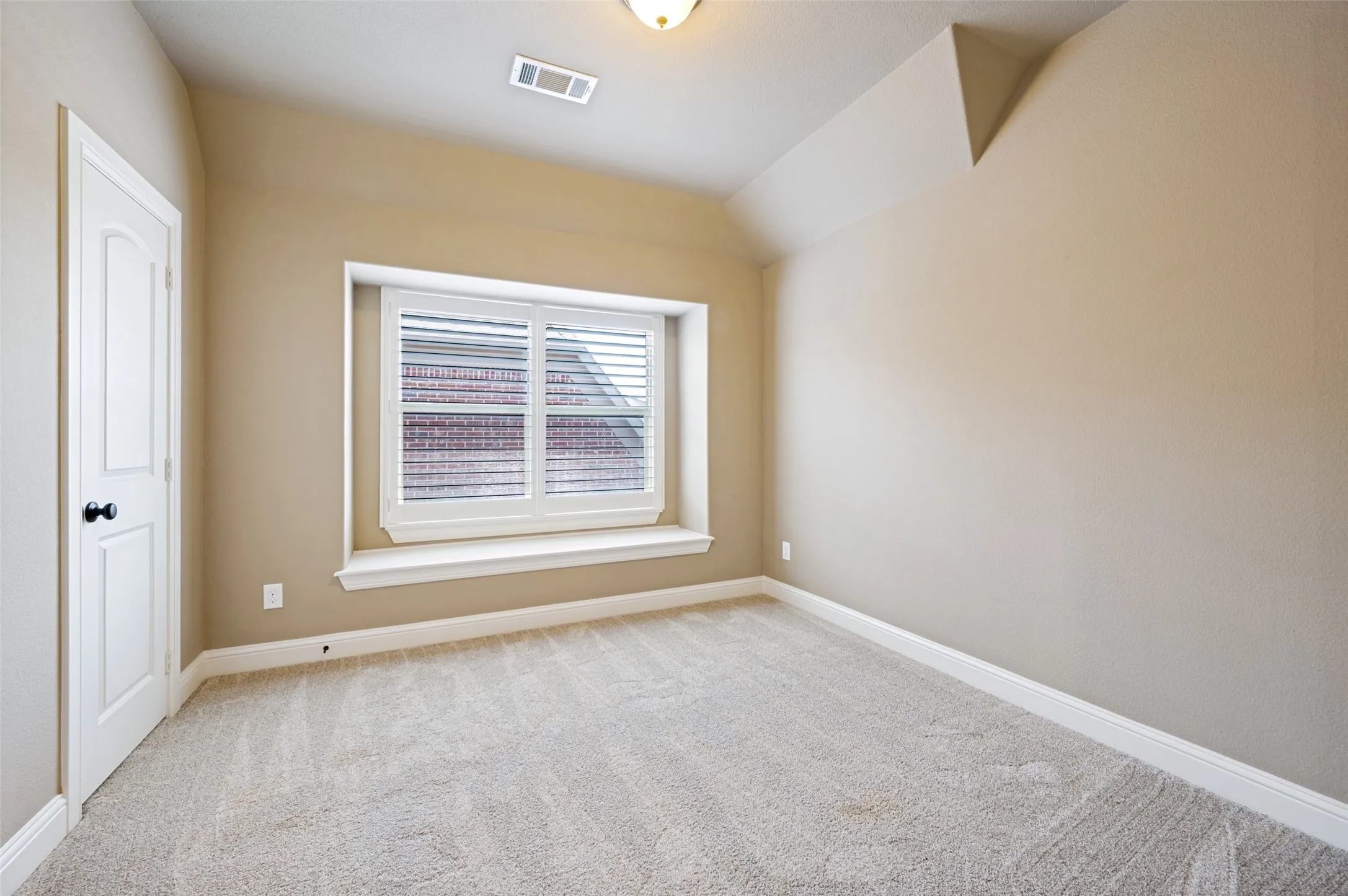 Bright, light-filled bedroom featuring neutral carpeting, recessed ceiling lighting, and a large double-hung window with white trim and interior shutters