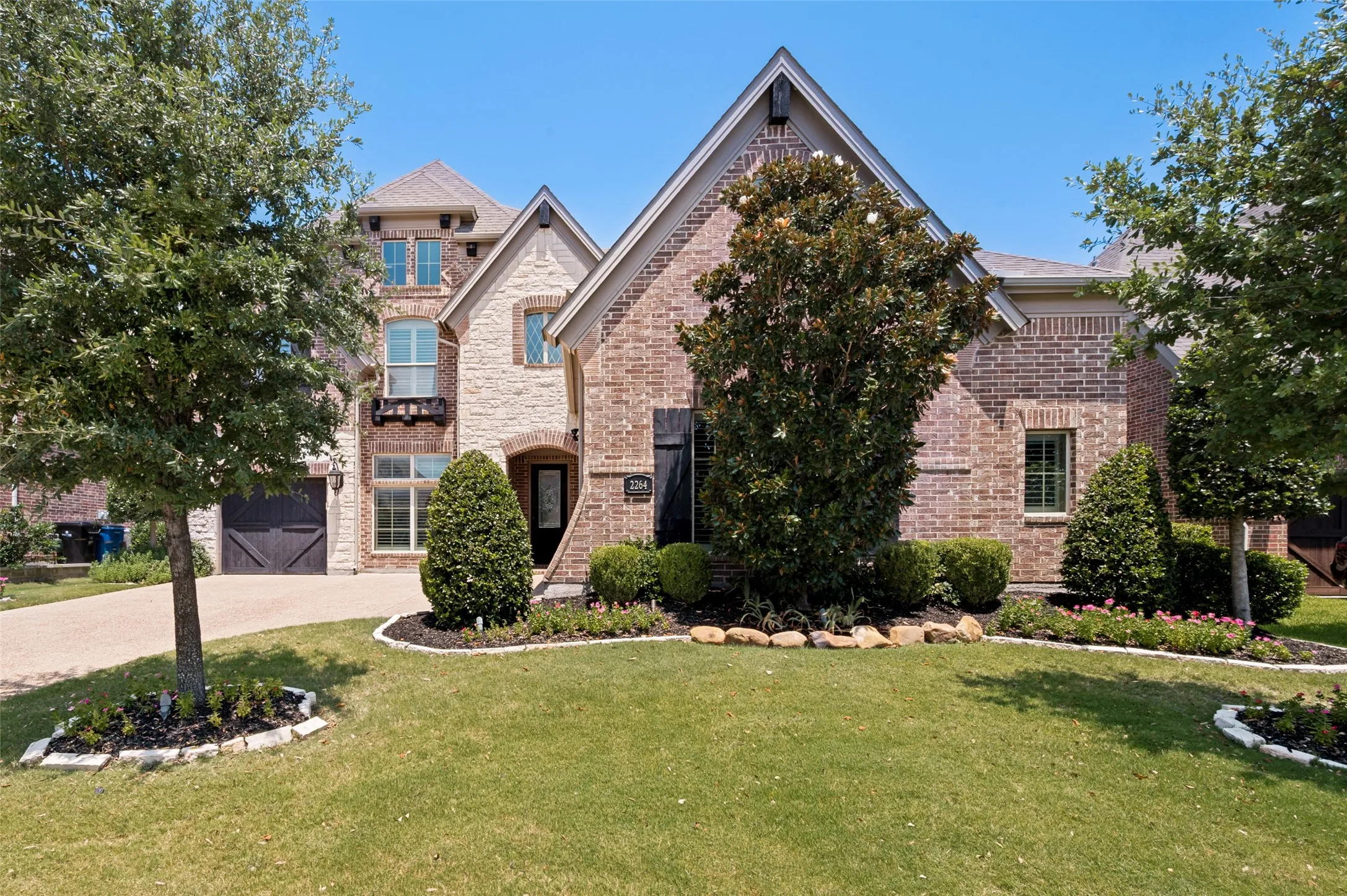 Elegant brick Colonial featuring a sophisticated exterior with peaked gable rooflines, arched entryway, and manicured landscaping