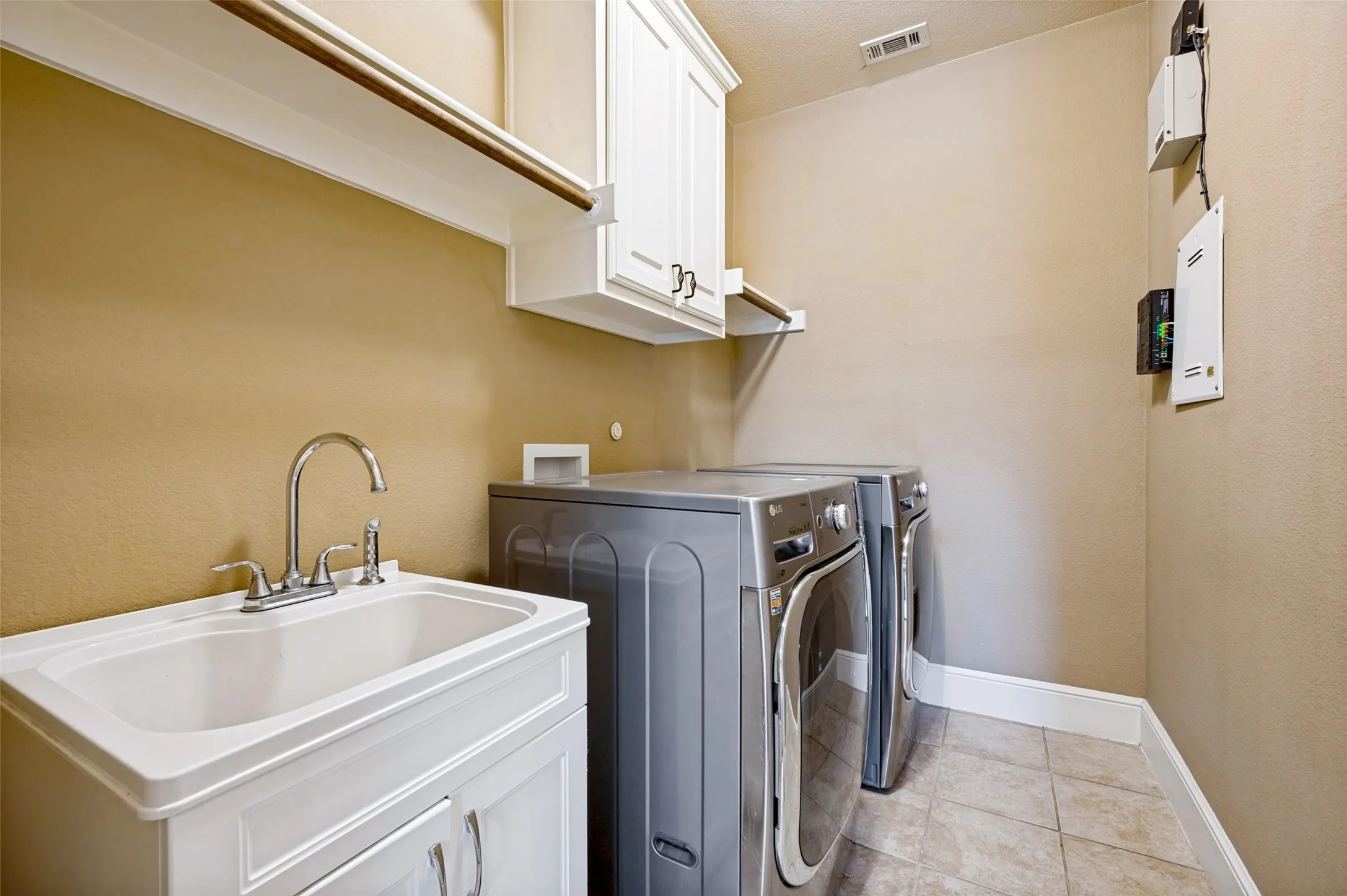 Utility room featuring a white laundry sink with chrome faucet, white cabinetry, a built-in hanging rod, and tile flooring