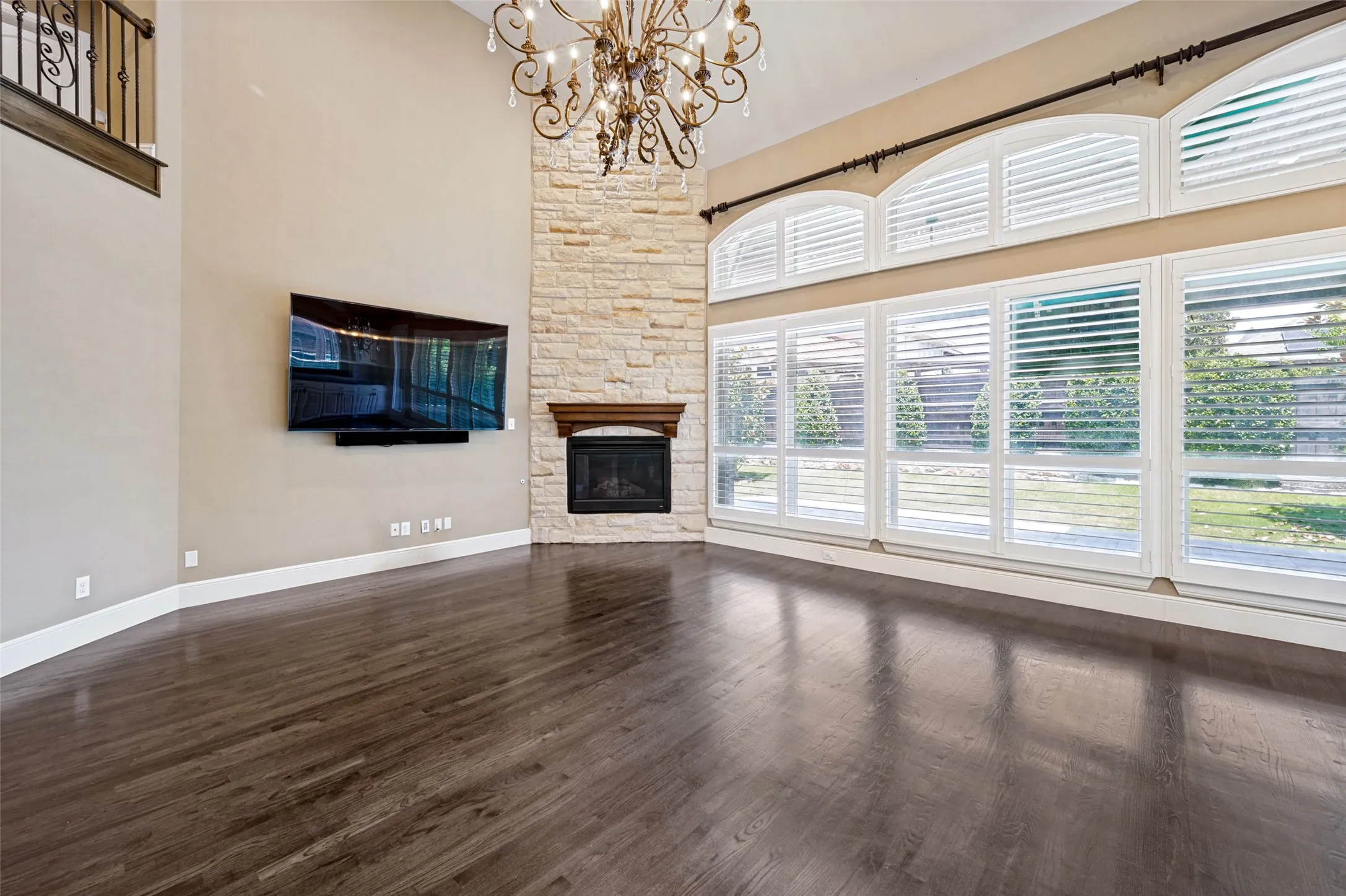 Spacious great room showcasing soaring ceilings, a corner fireplace with stone surround, and abundant natural light from expansive multi-pane windows and transom glazing
