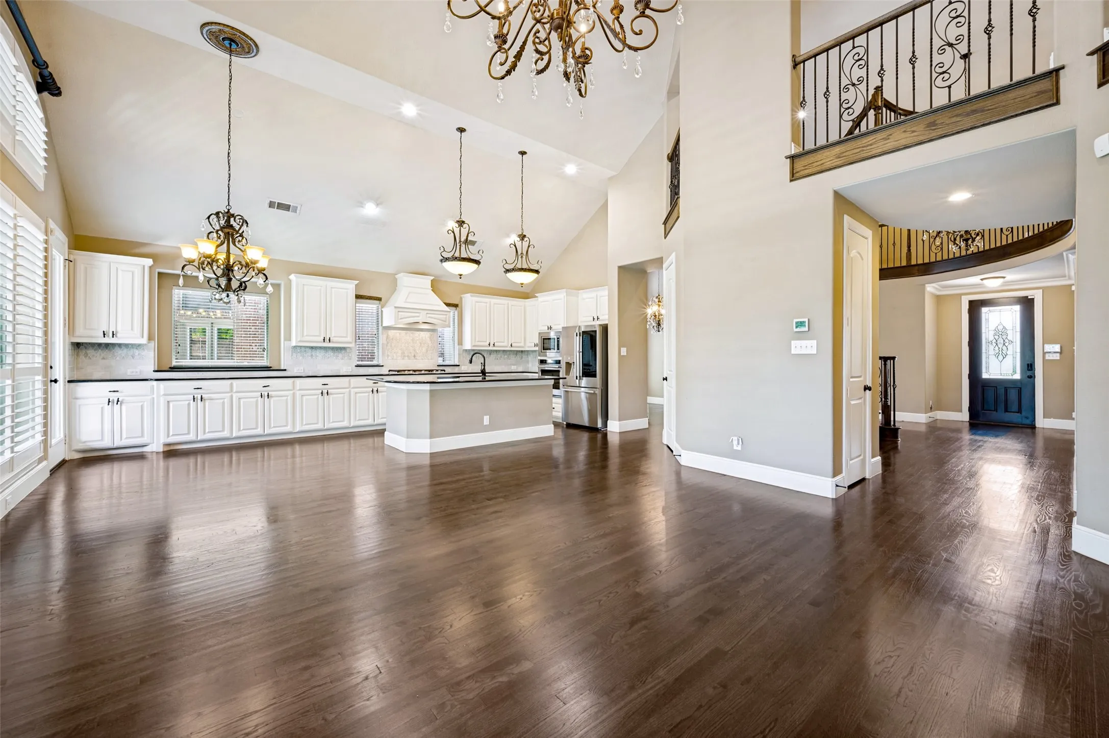 Open-concept living space featuring wood-finish flooring, a kitchen with white cabinetry and a central island, stainless steel appliances, and cathedral ceilings with chandelier lighting