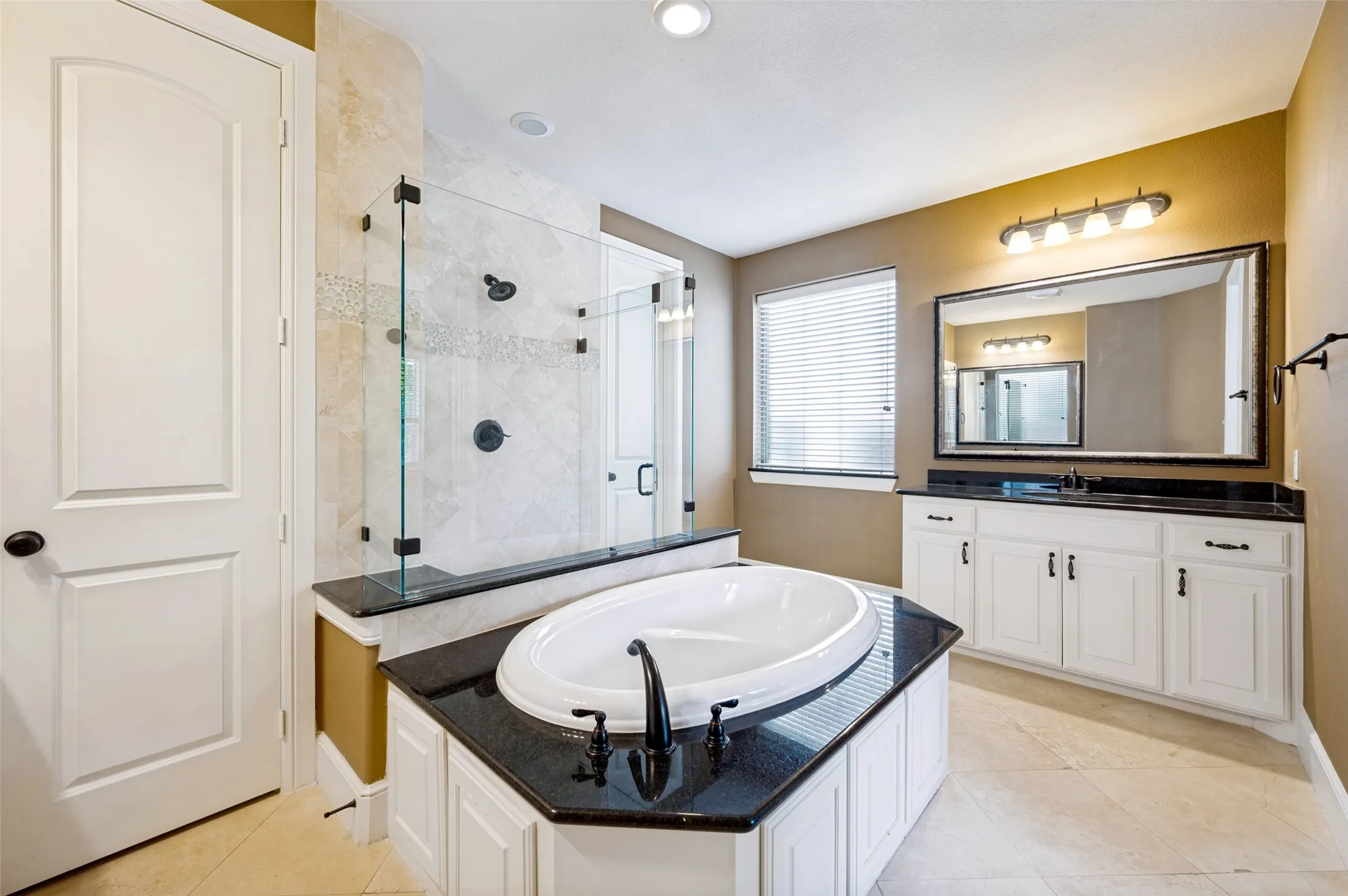 Bathroom featuring a built-in soaking tub with black countertop, a separate glass-enclosed shower with tiled surround, and a vanity with dual sinks, white cabinetry, and black countertop