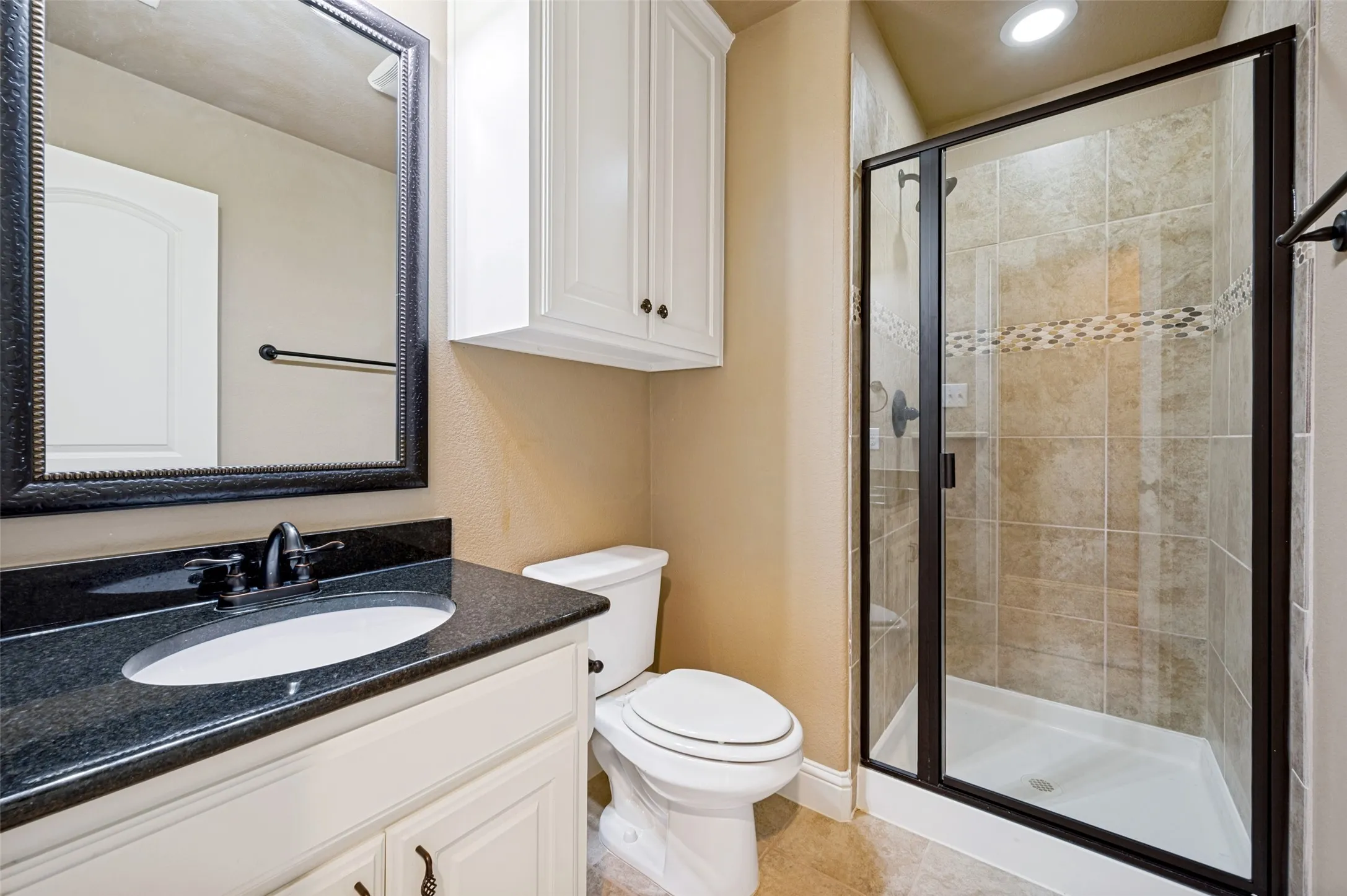 Bathroom featuring a dark granite countertop, a single vanity with white cabinetry, and an ornate framed mirror