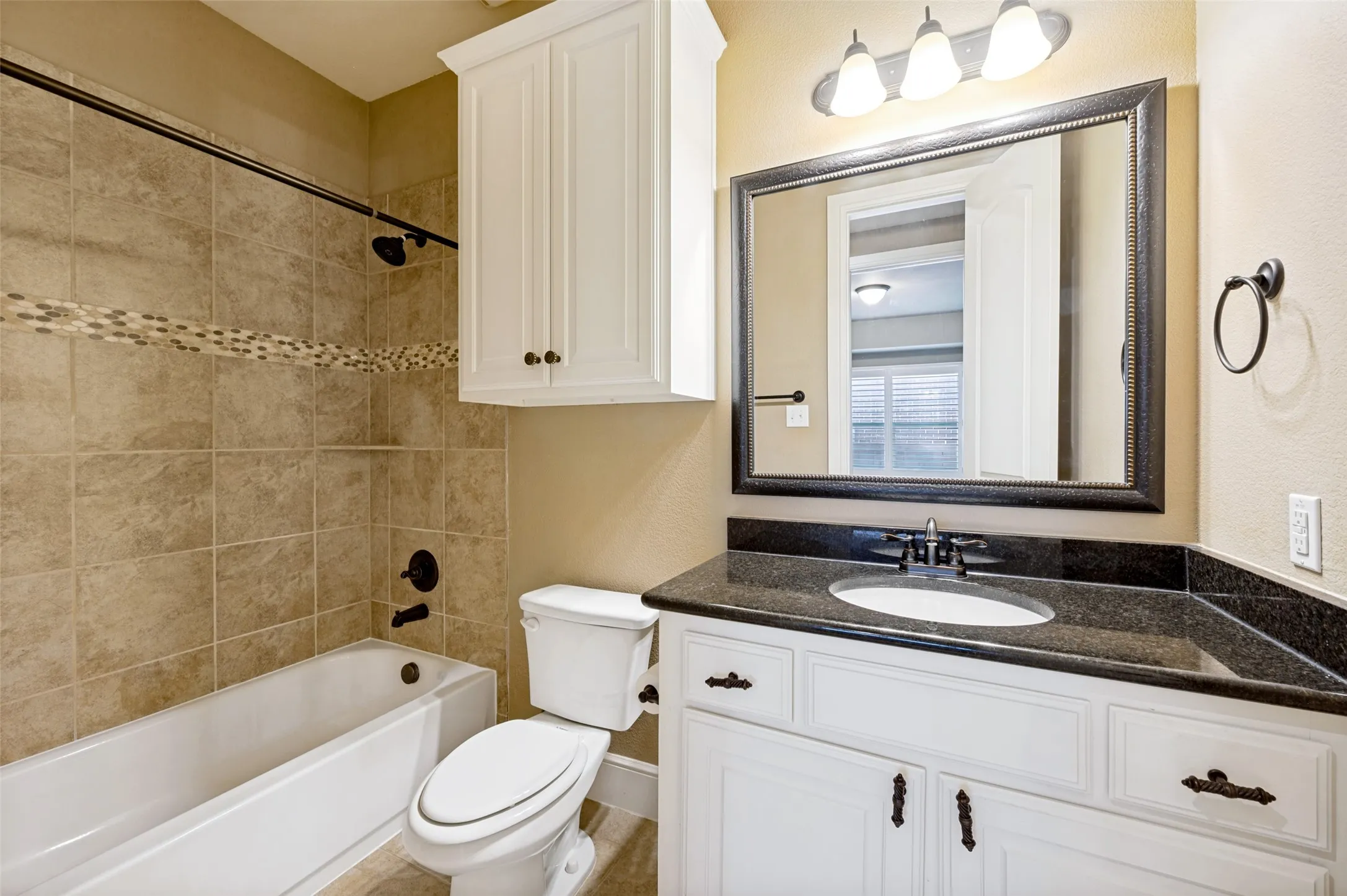 Bathroom featuring a white vanity with dark countertop, white under-mount sink, dark framed mirror, and a three-light fixture