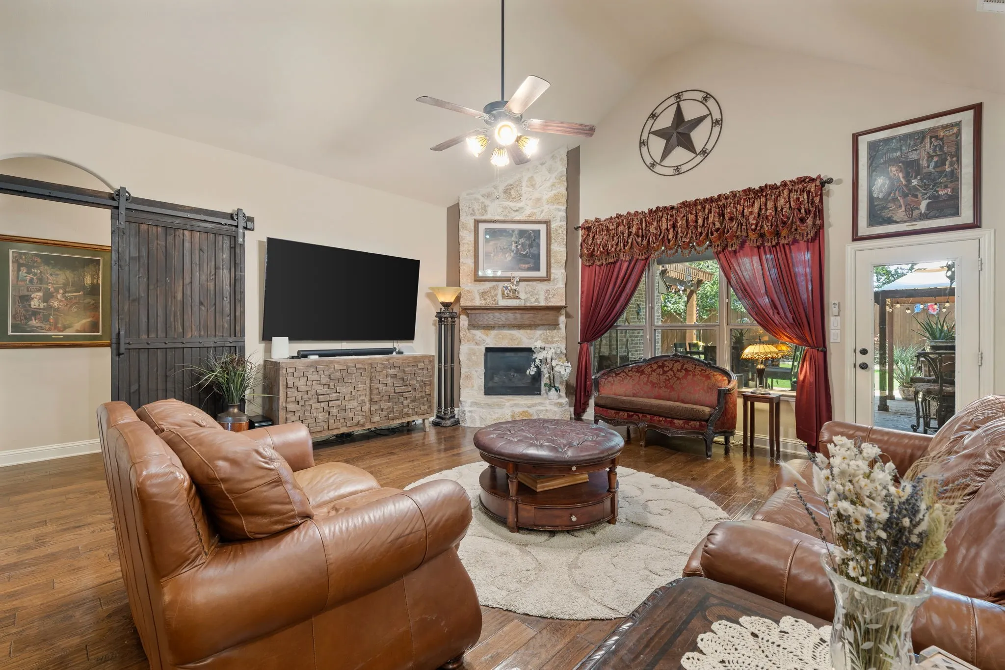 Living area featuring vaulted ceilings with a ceiling fan, stone-surround fireplace, wood-finish flooring, and a barn door entry