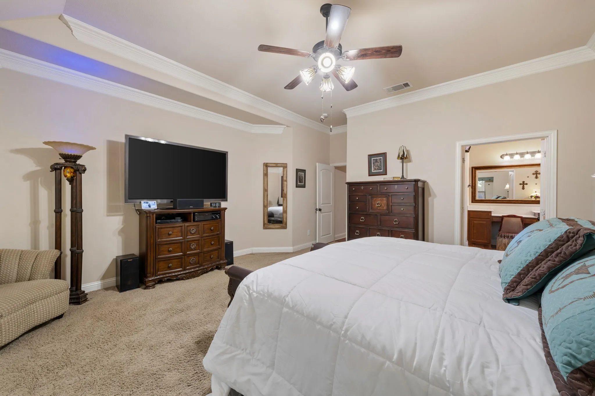 Spacious bedroom featuring neutral wall tones, crown molding, tray ceiling, and a ceiling fan with integrated lighting