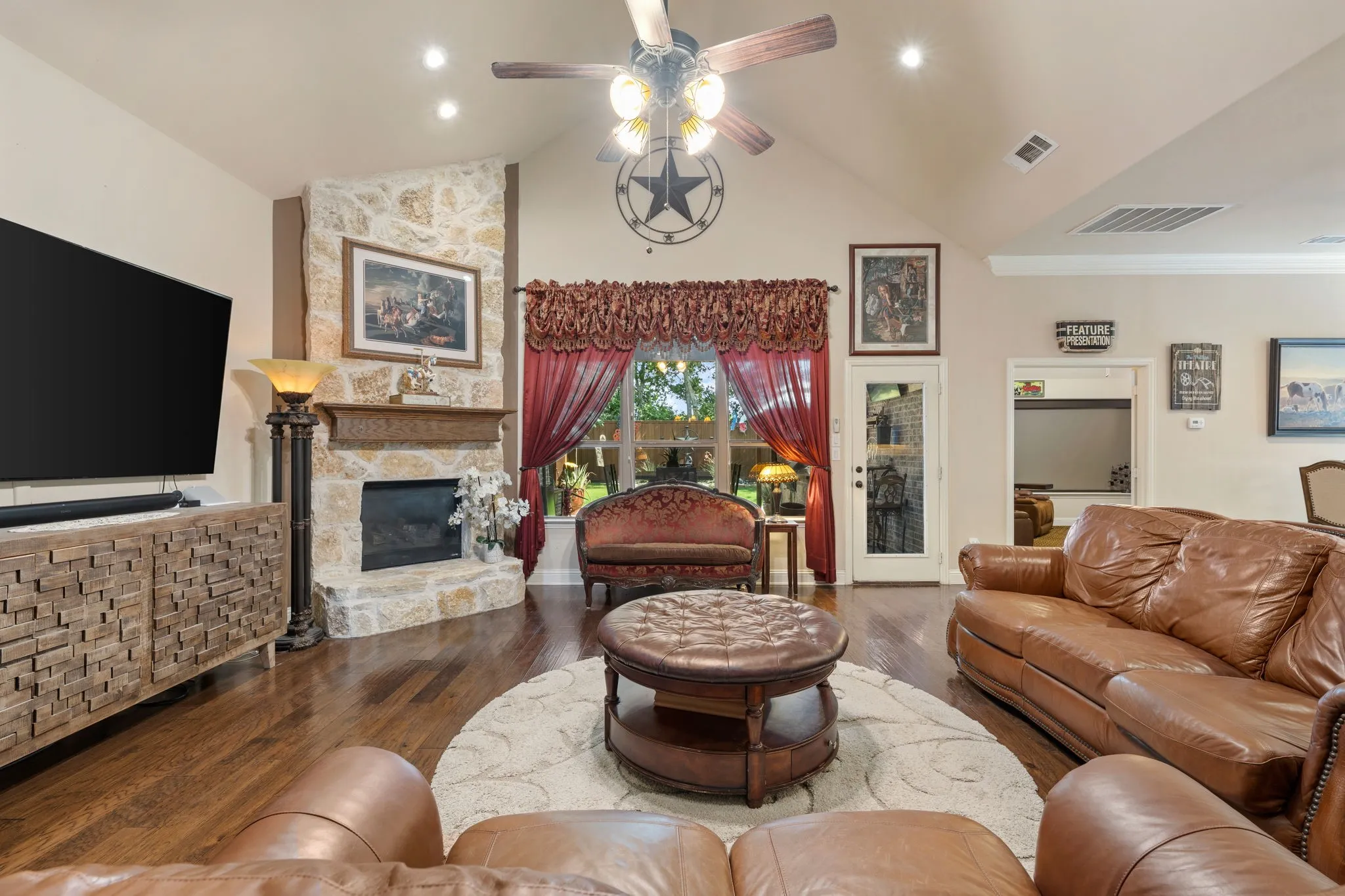 Living area featuring a vaulted ceiling with recessed lighting and a ceiling fan, wood-finish flooring, and a stone fireplace with a substantial mantel