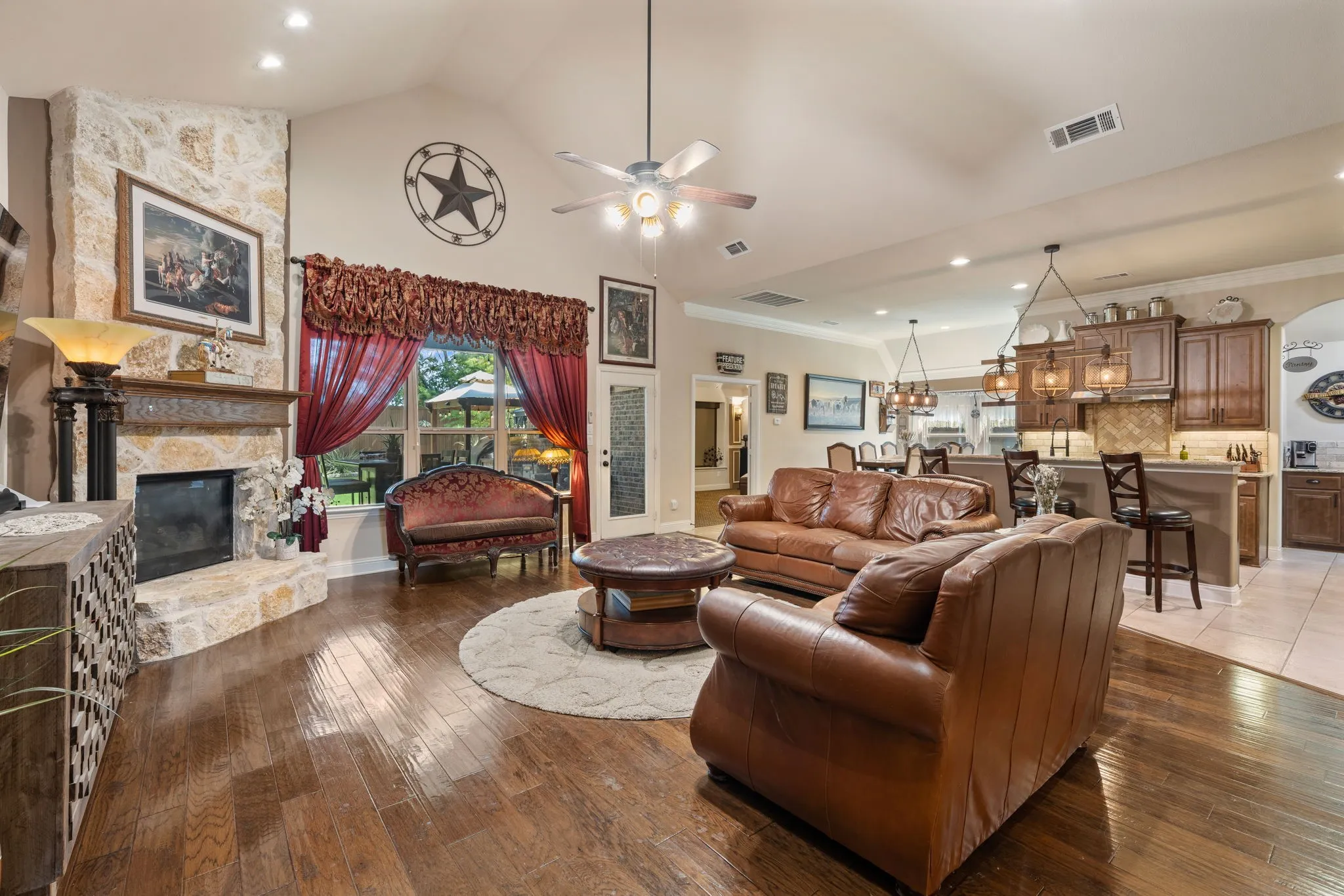 Expansive living space featuring a stone-clad corner fireplace with a wood mantel, wood-finish flooring, and a vaulted ceiling