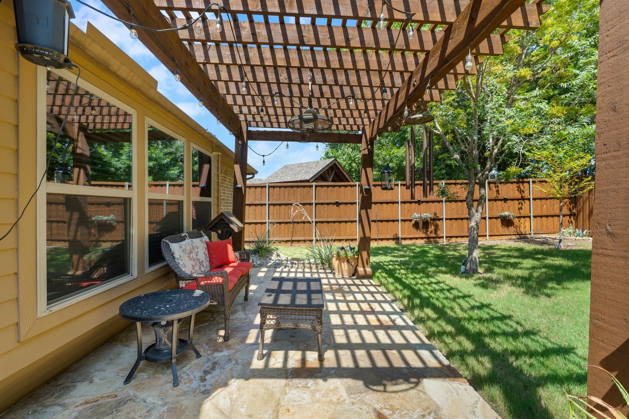 Expansive outdoor patio featuring a wooden pergola, string lighting, and flagstone paving