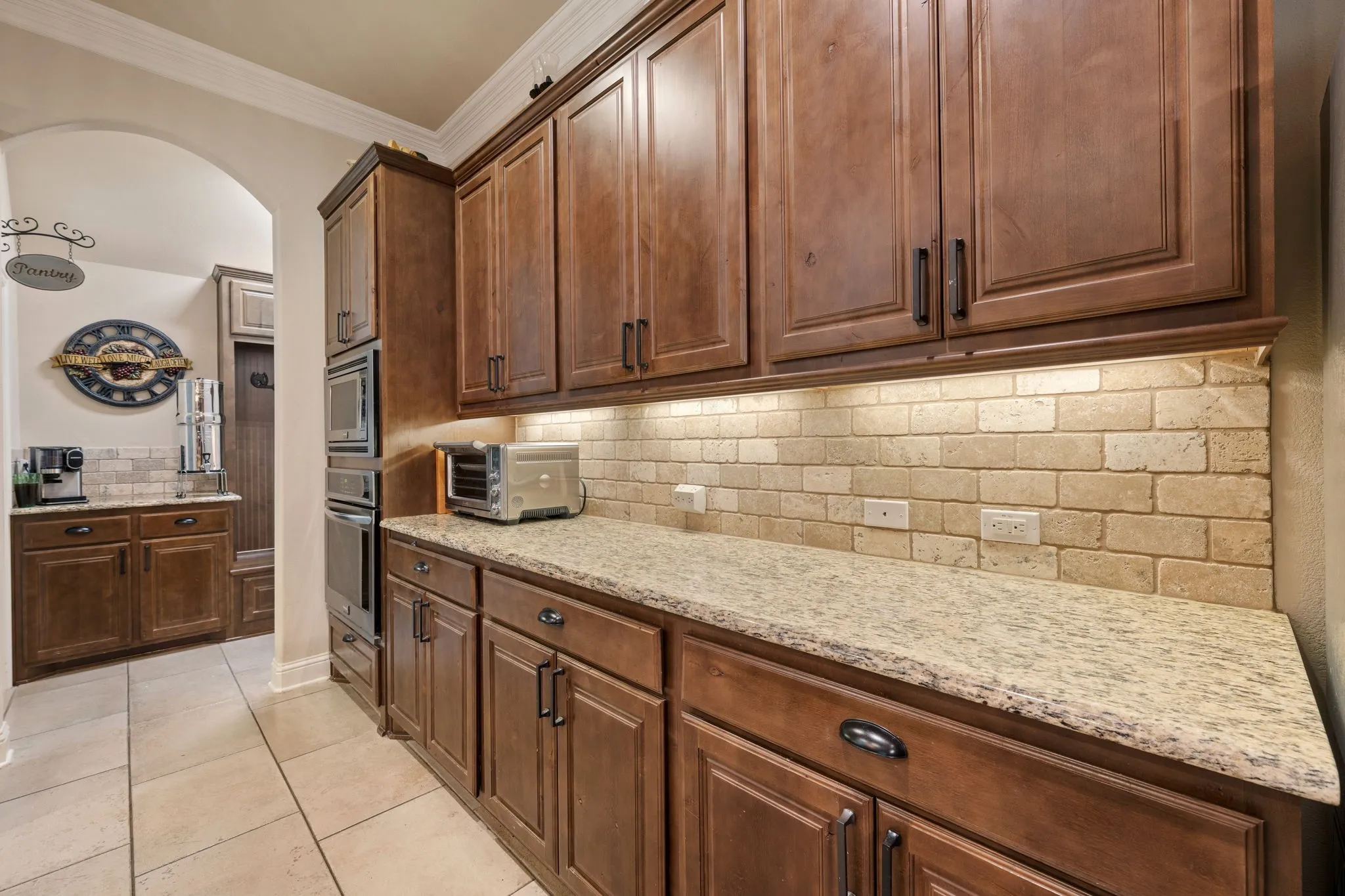 Built-in stainless steel oven and microwave, under-cabinet lighting, and stone backsplash