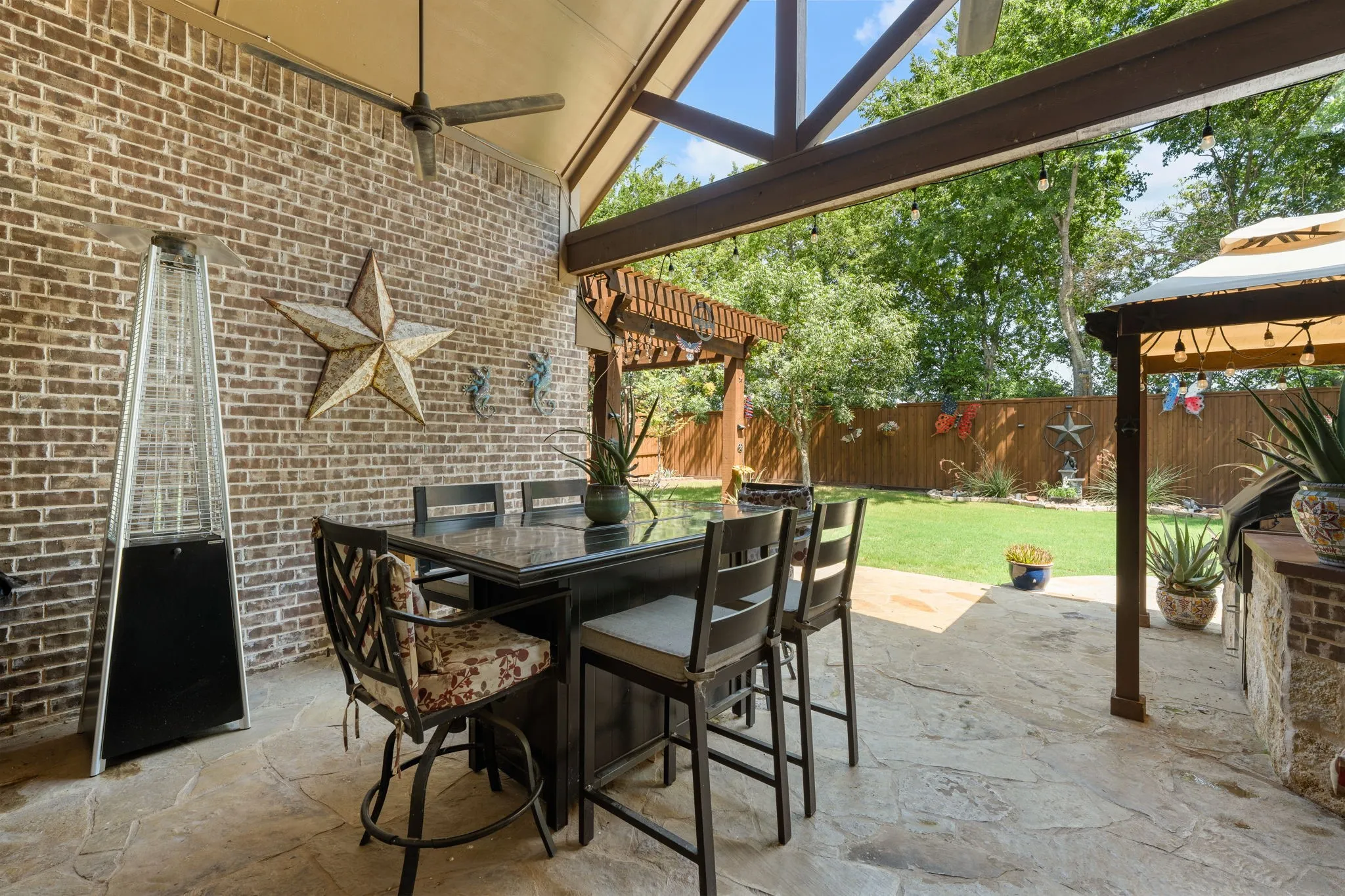 Covered outdoor patio featuring a flagstone floor, brick accent wall, ceiling fan, and exposed wood beams