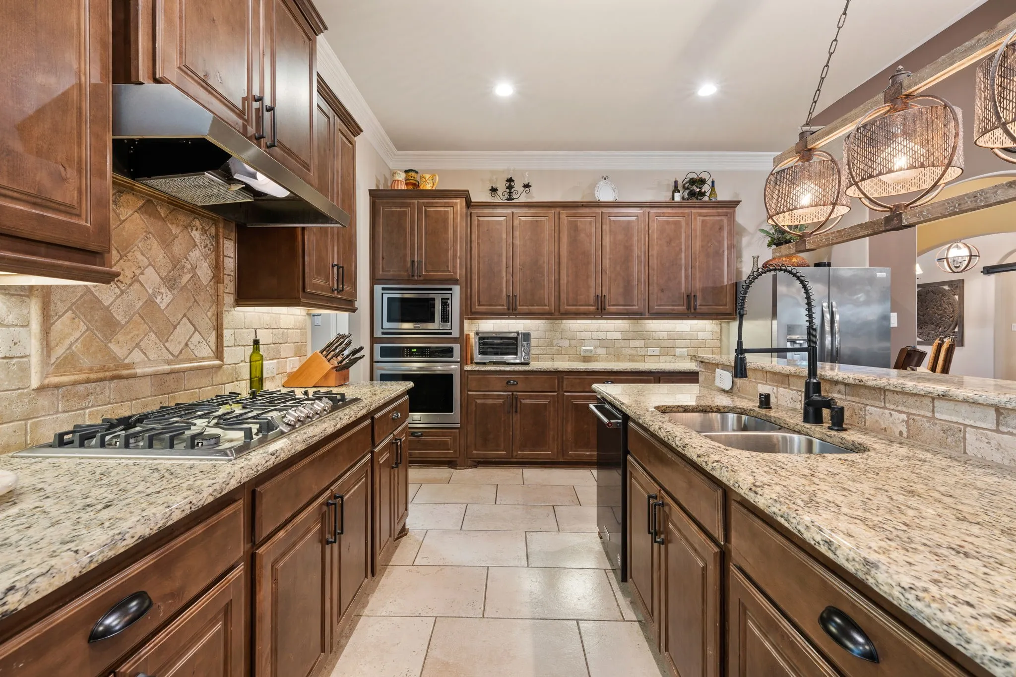 Kitchen featuring rich wood cabinetry, granite countertops, a gas cooktop, stainless steel built-in appliances, and a herringbone pattern tile backsplash