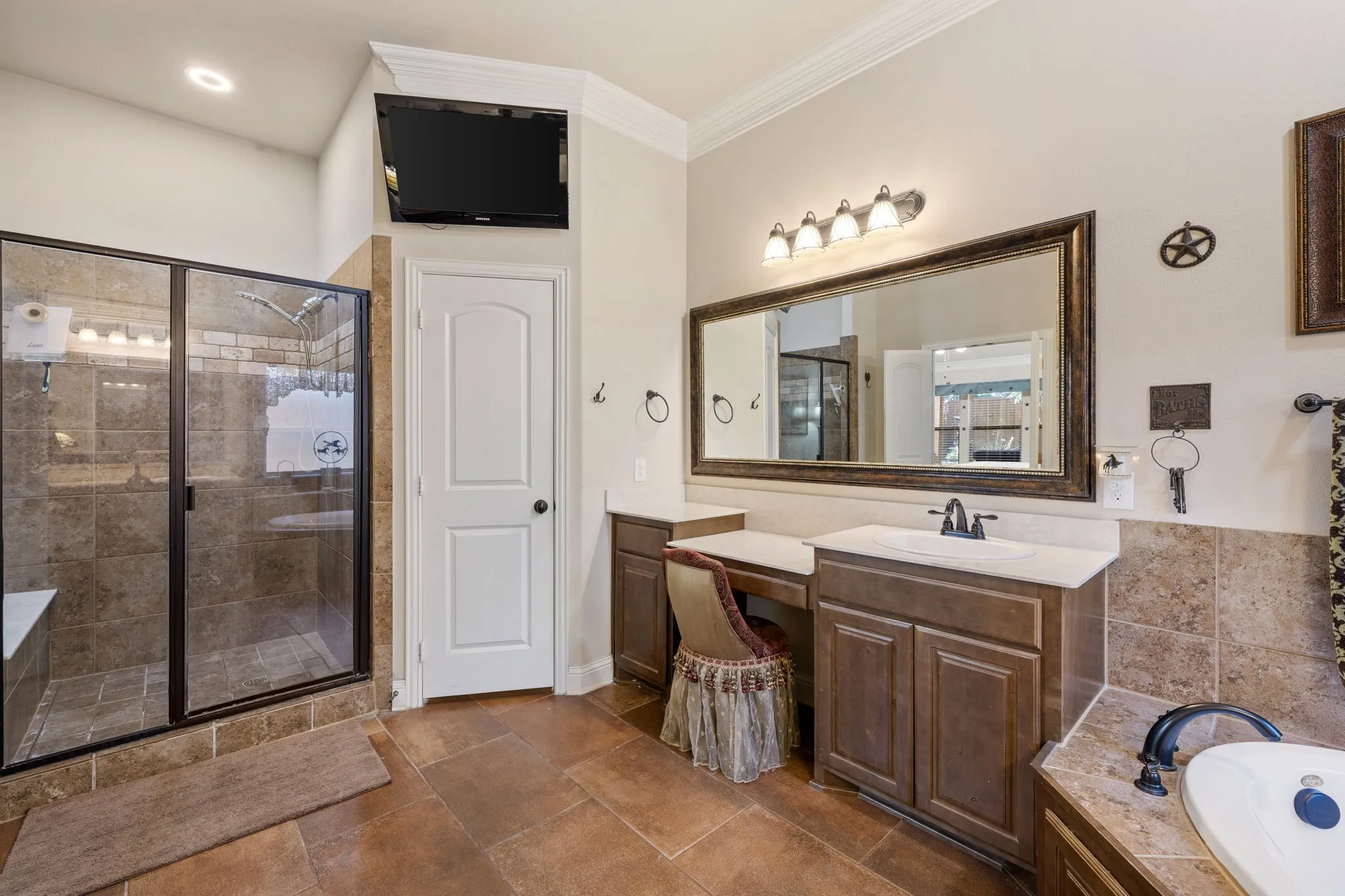 Spacious bathroom featuring a glass-enclosed shower with tiled surround, a built-in vanity with single sink and countertop, and a separate makeup vanity