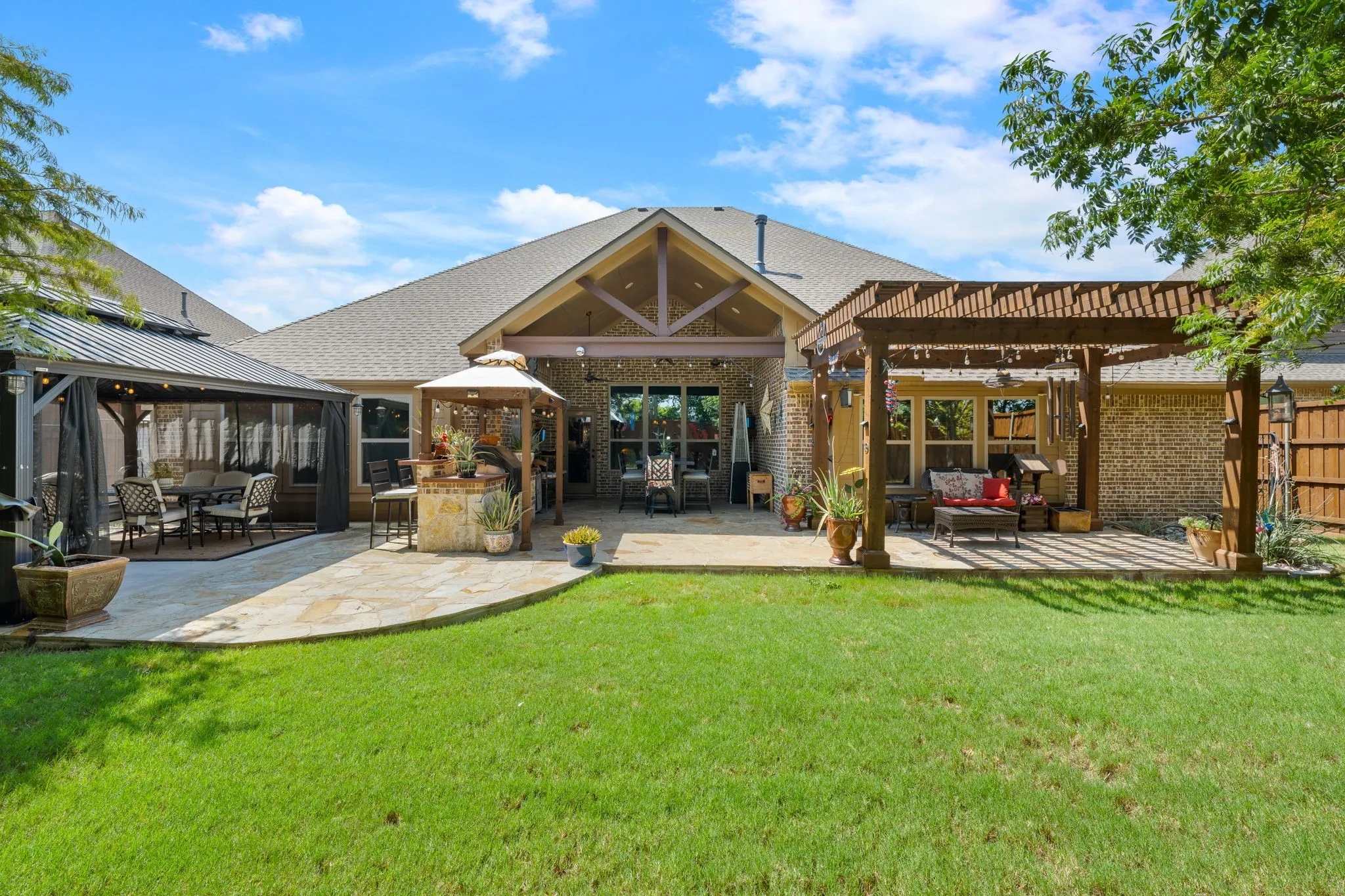 Expansive backyard featuring a stone patio, covered gazebo with screening, and a pergola-covered outdoor sitting area