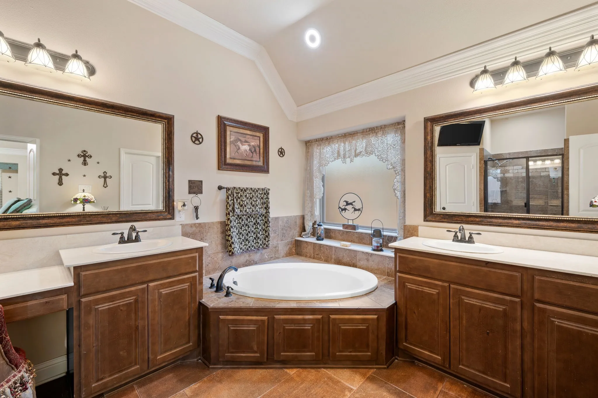 Bathroom featuring a built-in corner soaking tub, dual vanities with integrated sinks, wood cabinetry, and tiled flooring