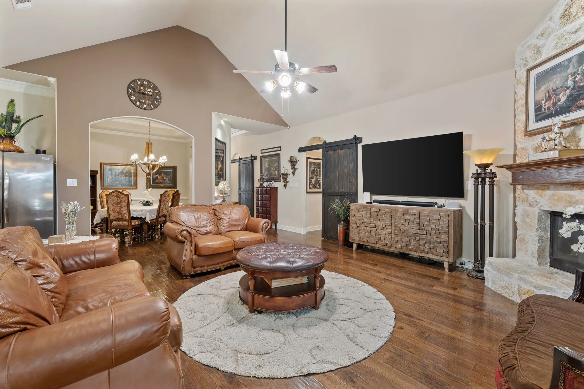 Spacious living area featuring wood-finish flooring, a stone fireplace, and vaulted ceilings