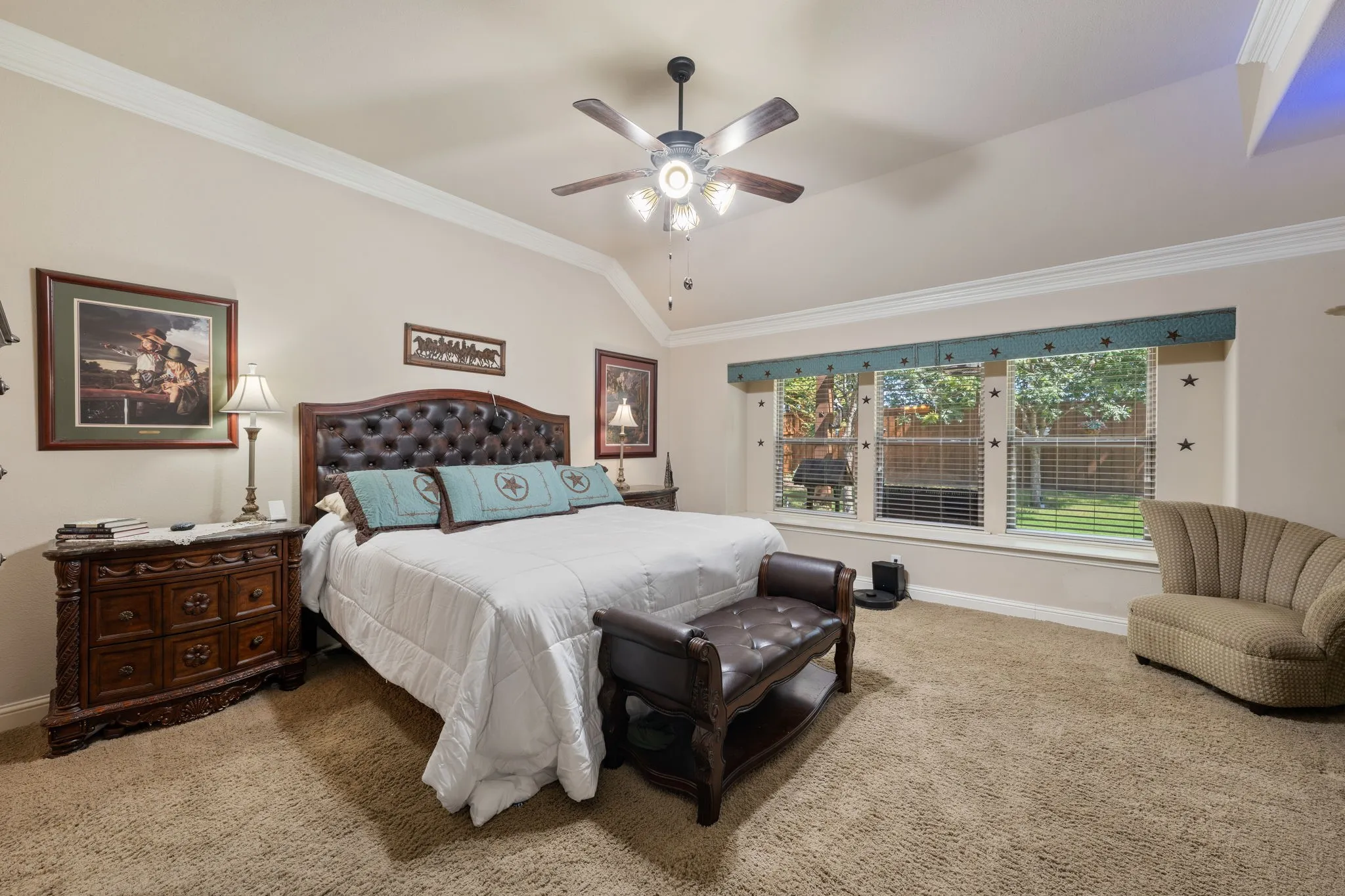 Carpeted room featuring a tufted leather headboard, crown molding, a ceiling fan with integrated lighting, and multiple windows overlooking a fenced yard