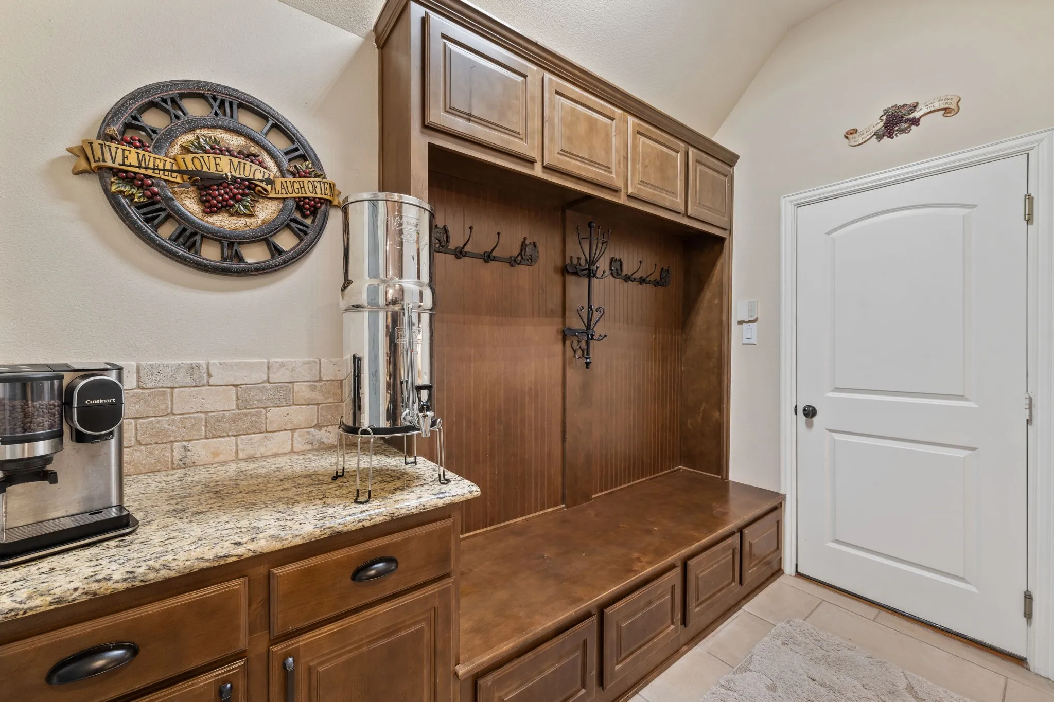 Built-in wood cabinetry with integrated coat hooks, an arched panel door, and tile flooring