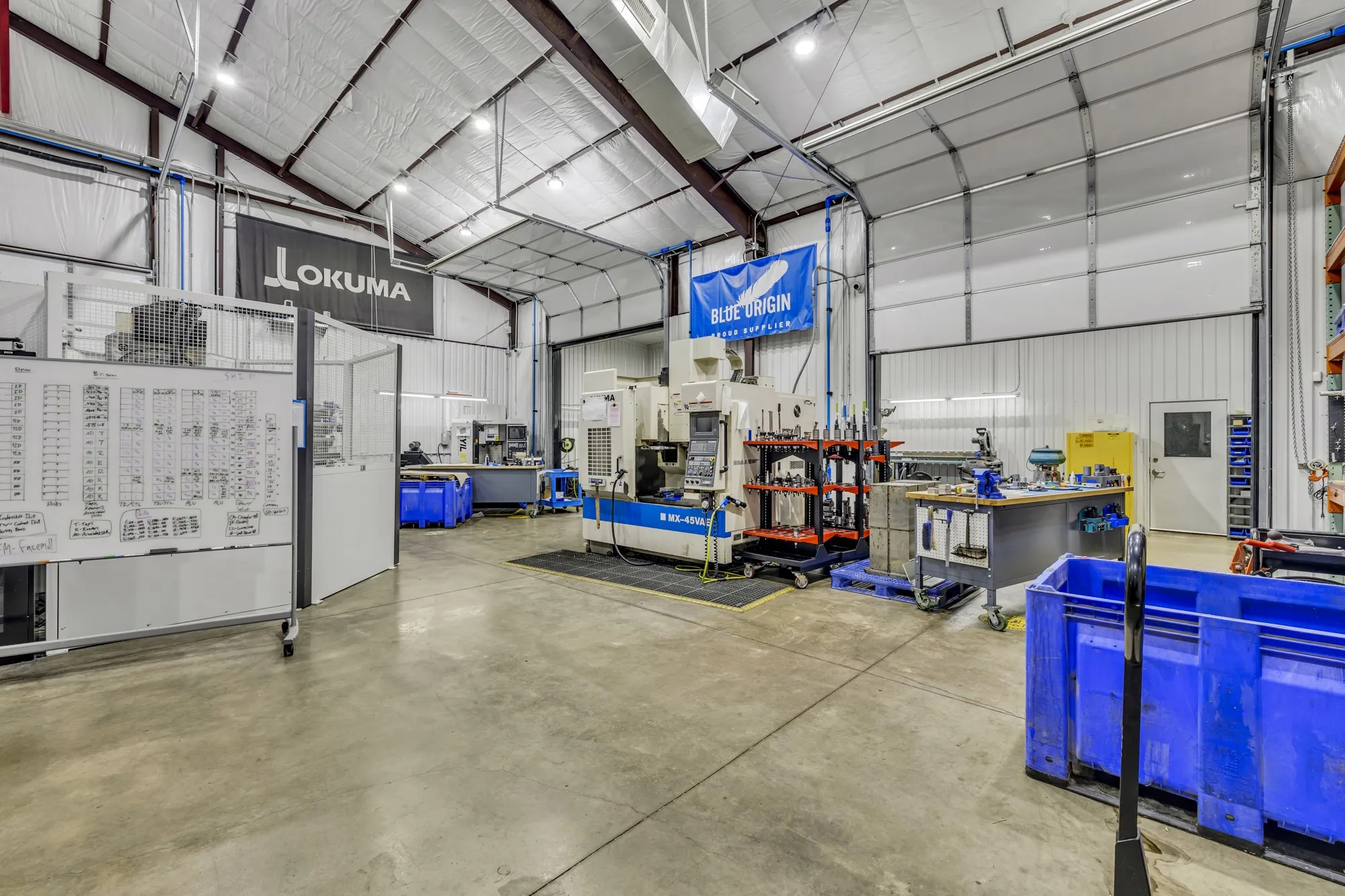 Spacious industrial interior featuring a high-pitched ceiling with exposed metal trusses, concrete flooring, and insulated white wall panels