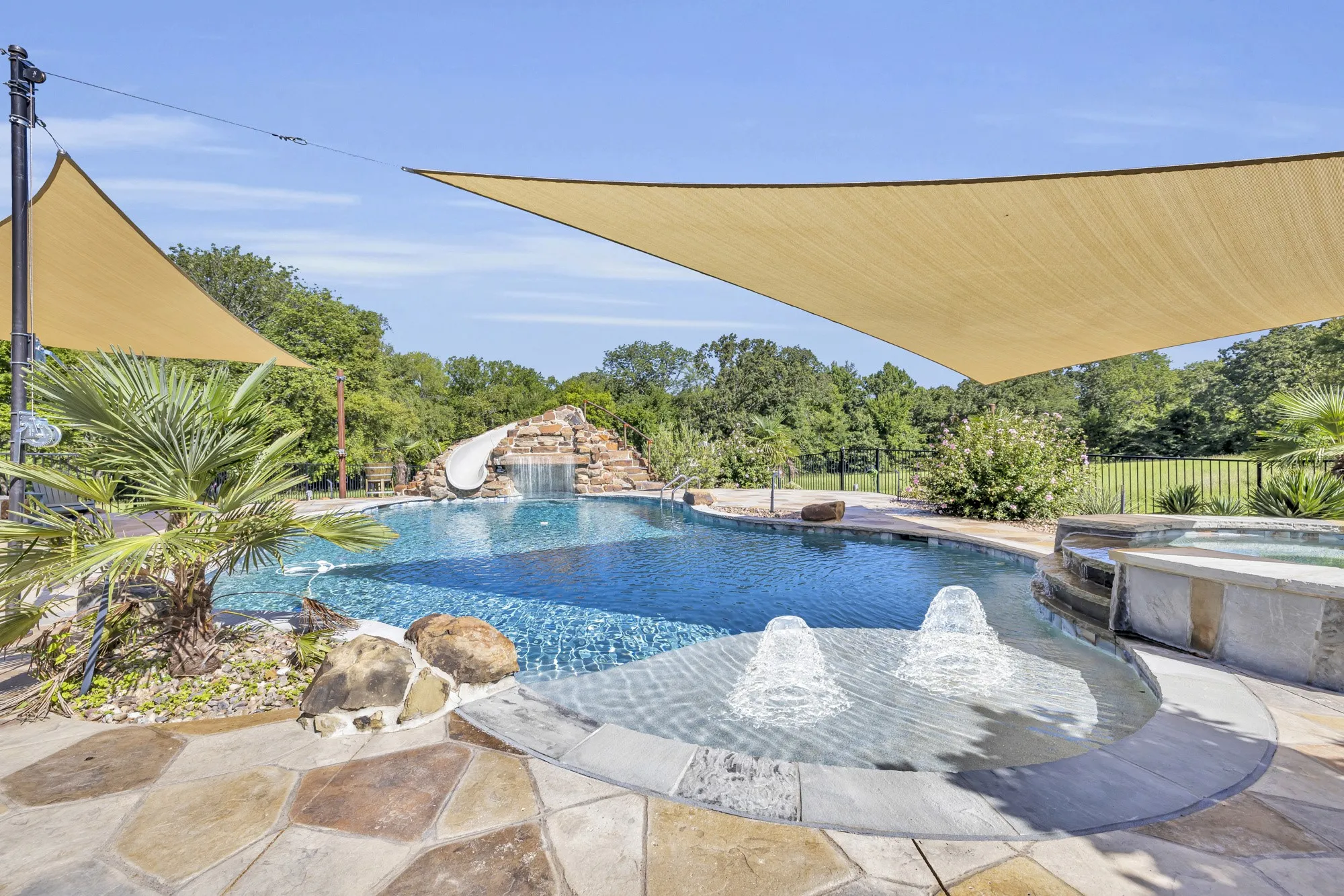 Custom-shaped swimming pool featuring a rock waterfall, built-in slide, and adjacent spa