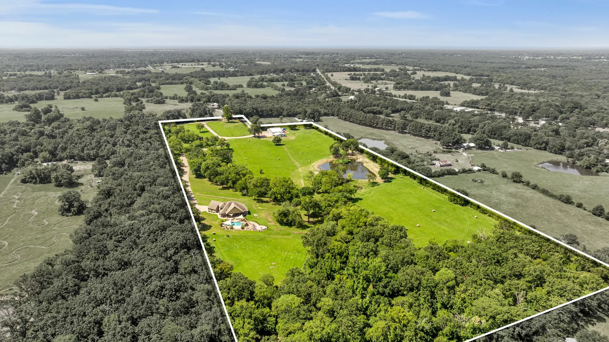 Expansive rural property featuring a primary residence with a swimming pool, a secondary structure, multiple ponds, and vast open fields bordered by mature trees