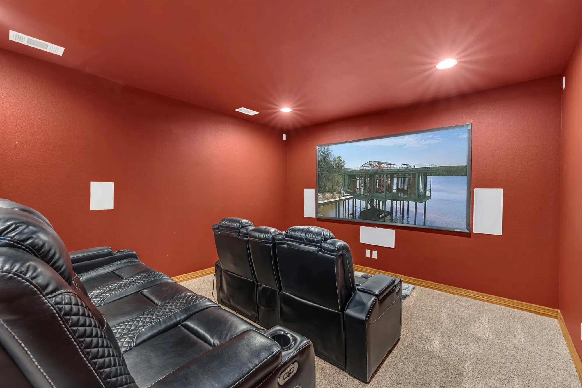 Dedicated media room featuring a large wall-mounted screen, recessed ceiling lighting, and integrated wall speakers
