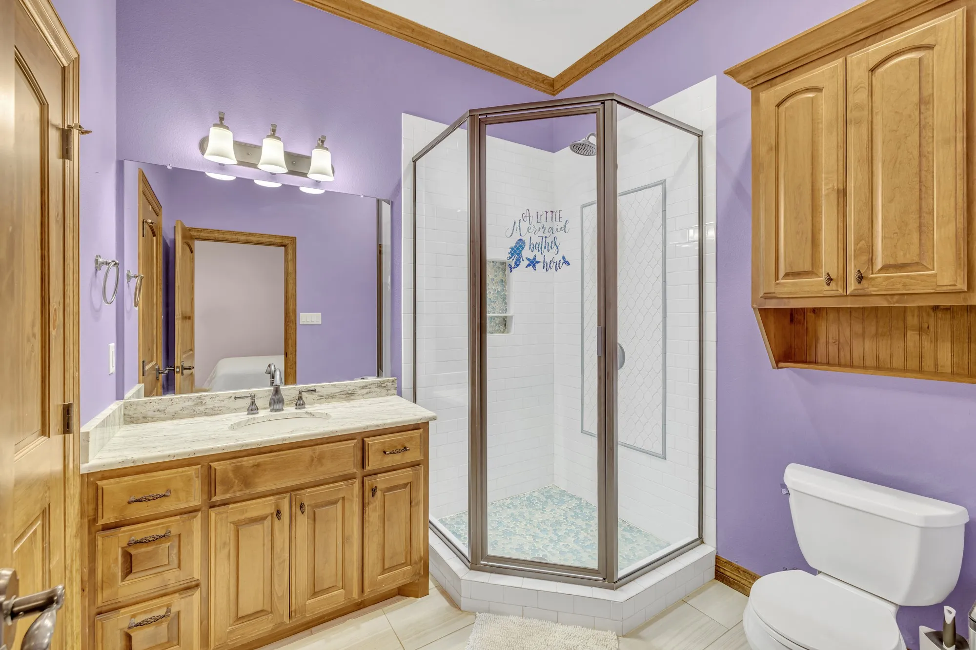 Bathroom featuring a stand-alone shower with glass enclosure and tiled interior, a single vanity with wood cabinetry and a light-toned countertop, and an overhead vanity light fixture