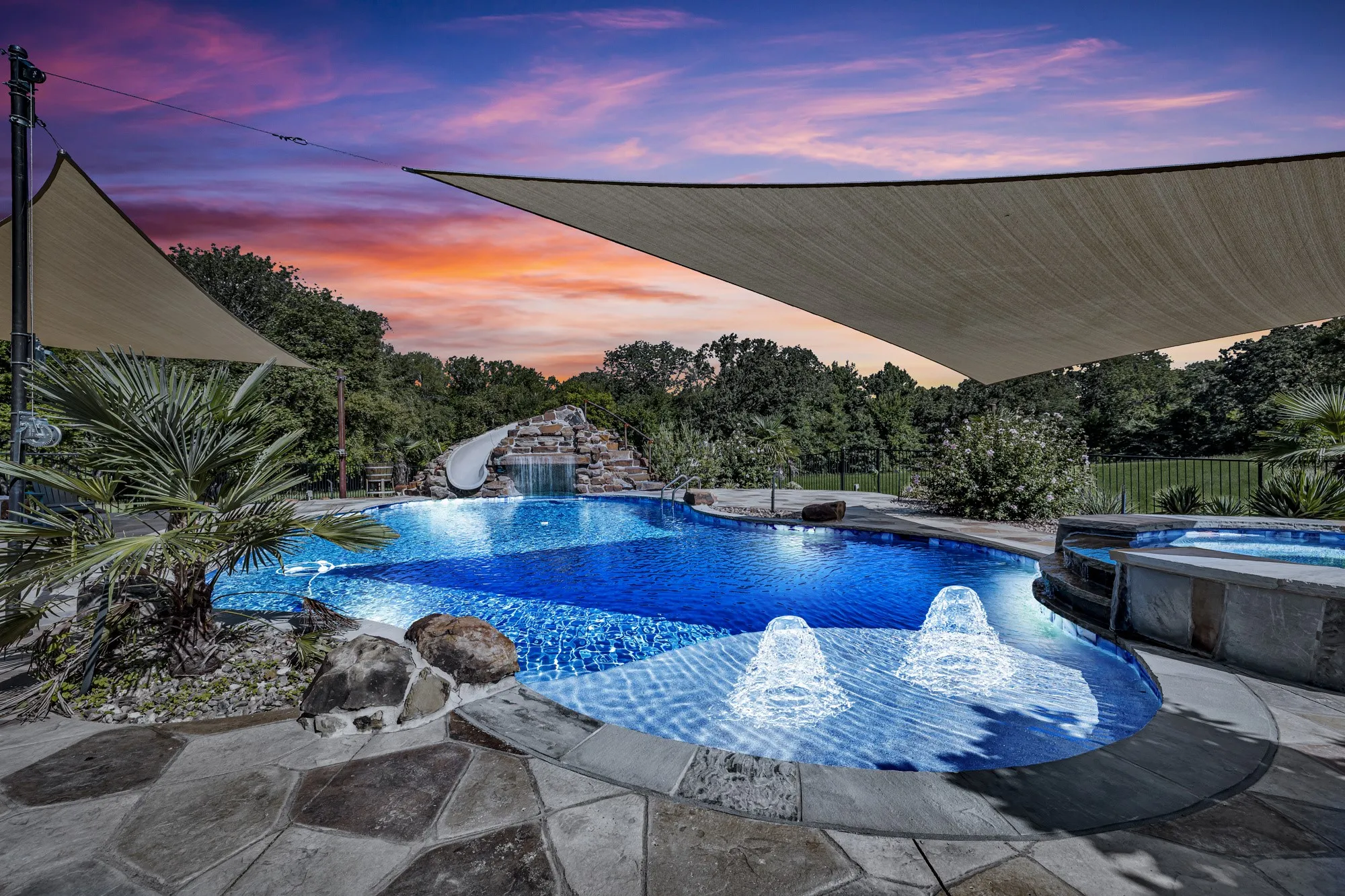 Custom-shaped swimming pool with an integrated spa, rock waterfall feature, and two in-pool fountains