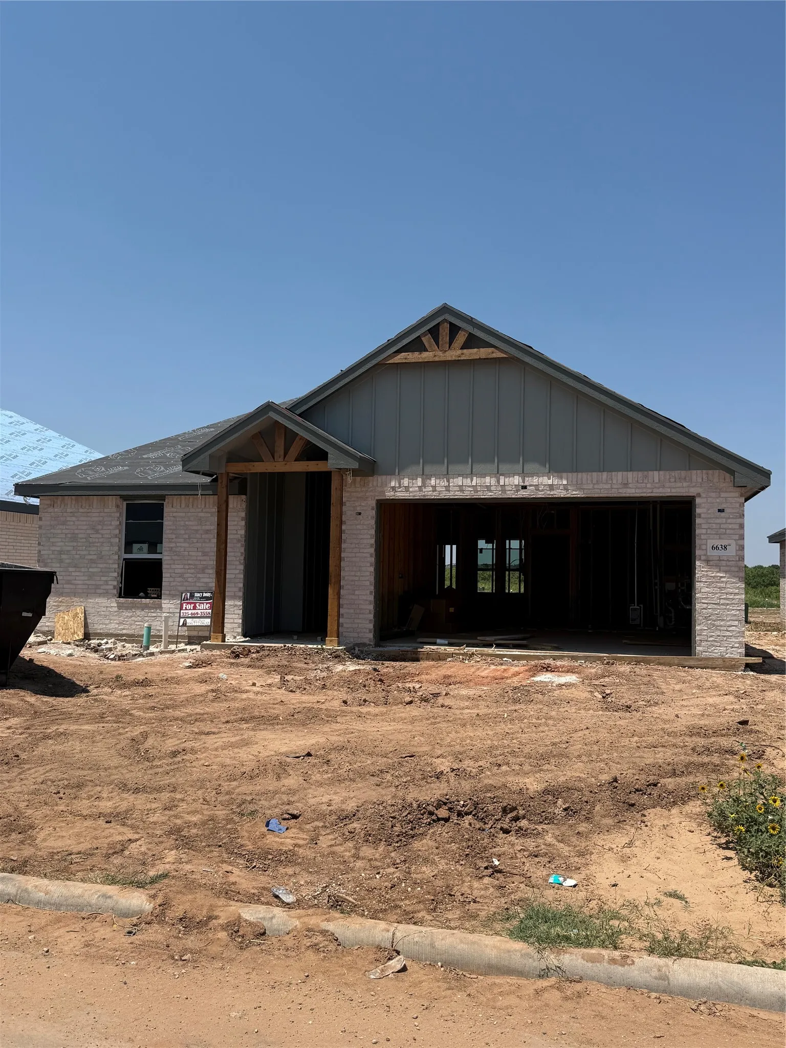 Single-story residence featuring light-colored brick exterior, a covered entryway with wood-finish columns, a prominent gabled roofline with vertical siding, and an integrated garage structure