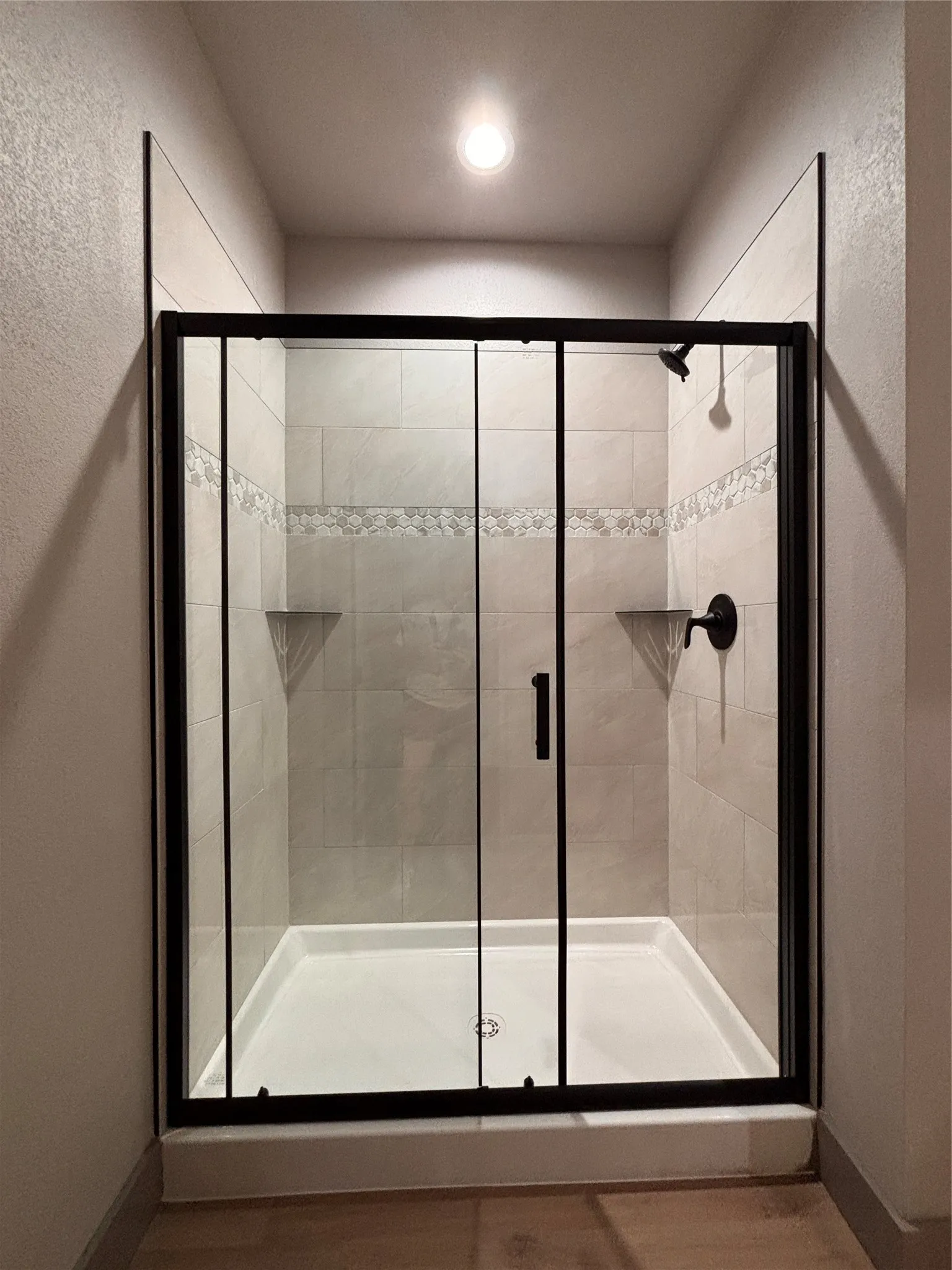 Enclosed shower featuring a clear glass door with black framing, tiled walls with an accent band, two built-in corner shelves, and matte black fixtures