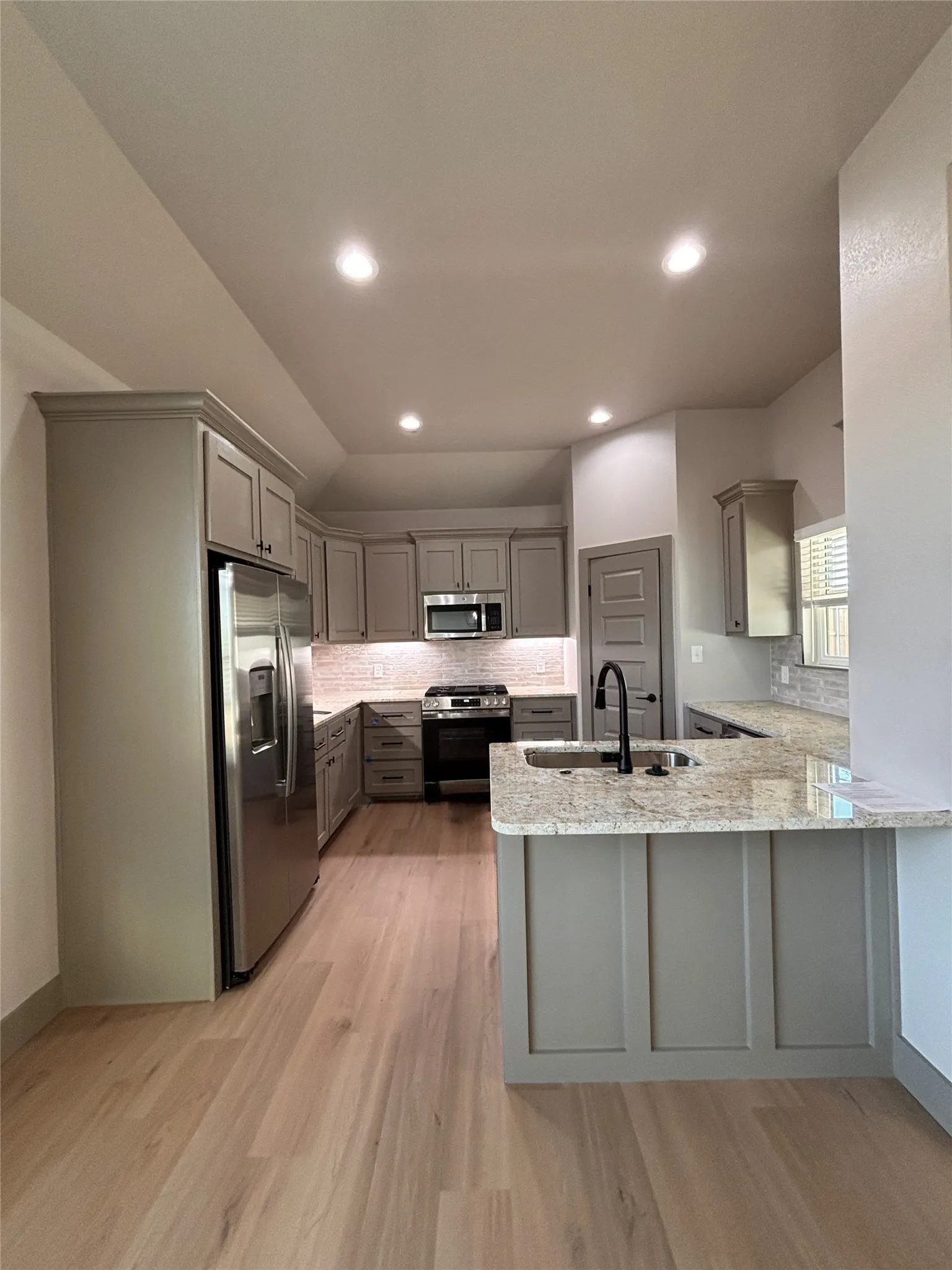 Modern kitchen featuring light wood-finish flooring, recessed lighting, stainless steel appliances, a light-toned backsplash, and light-colored cabinetry with a coordinating island