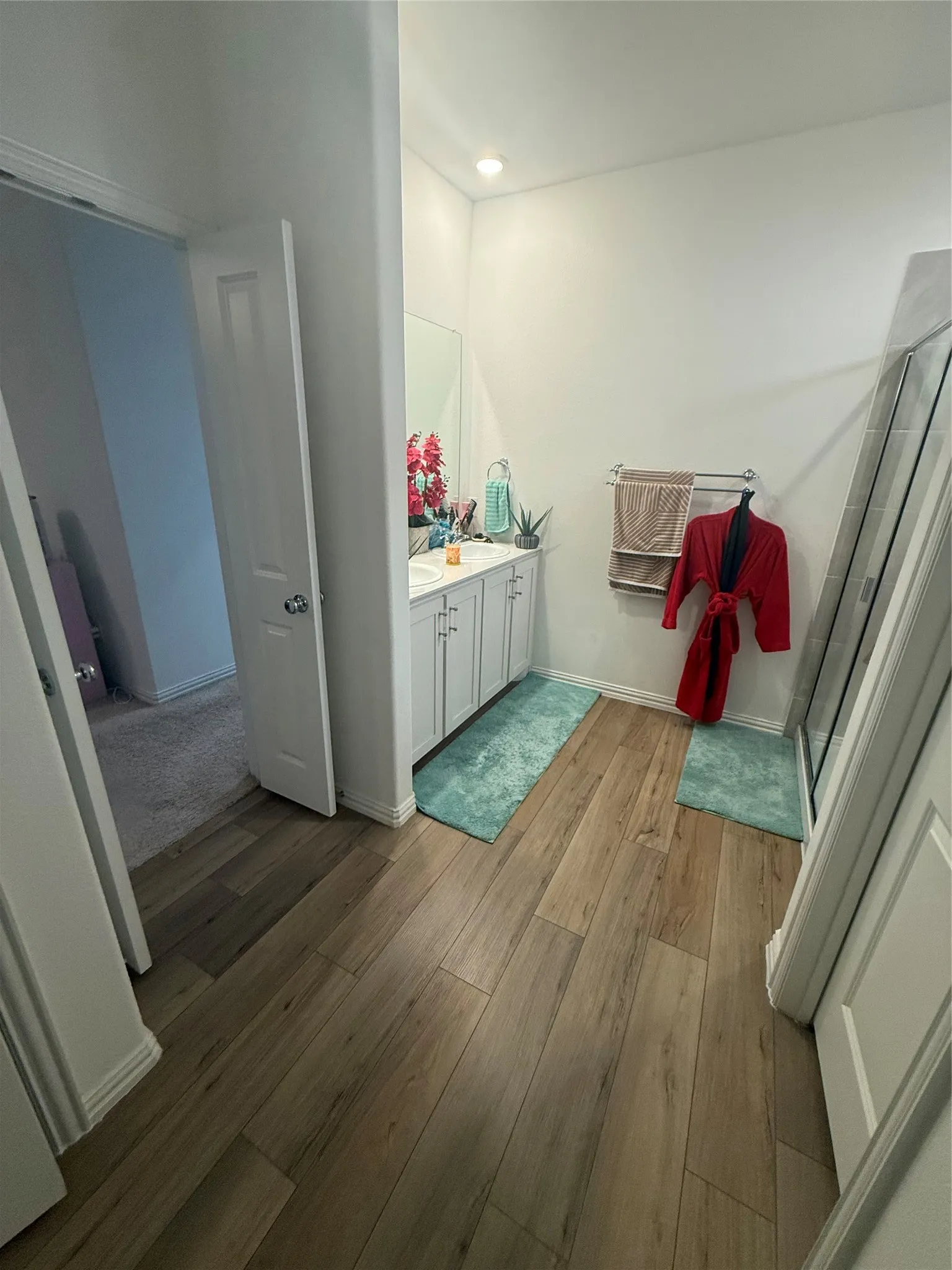 Bathroom featuring wood-finish flooring, a white vanity with dual sinks, a large mirror, and a glass-enclosed shower