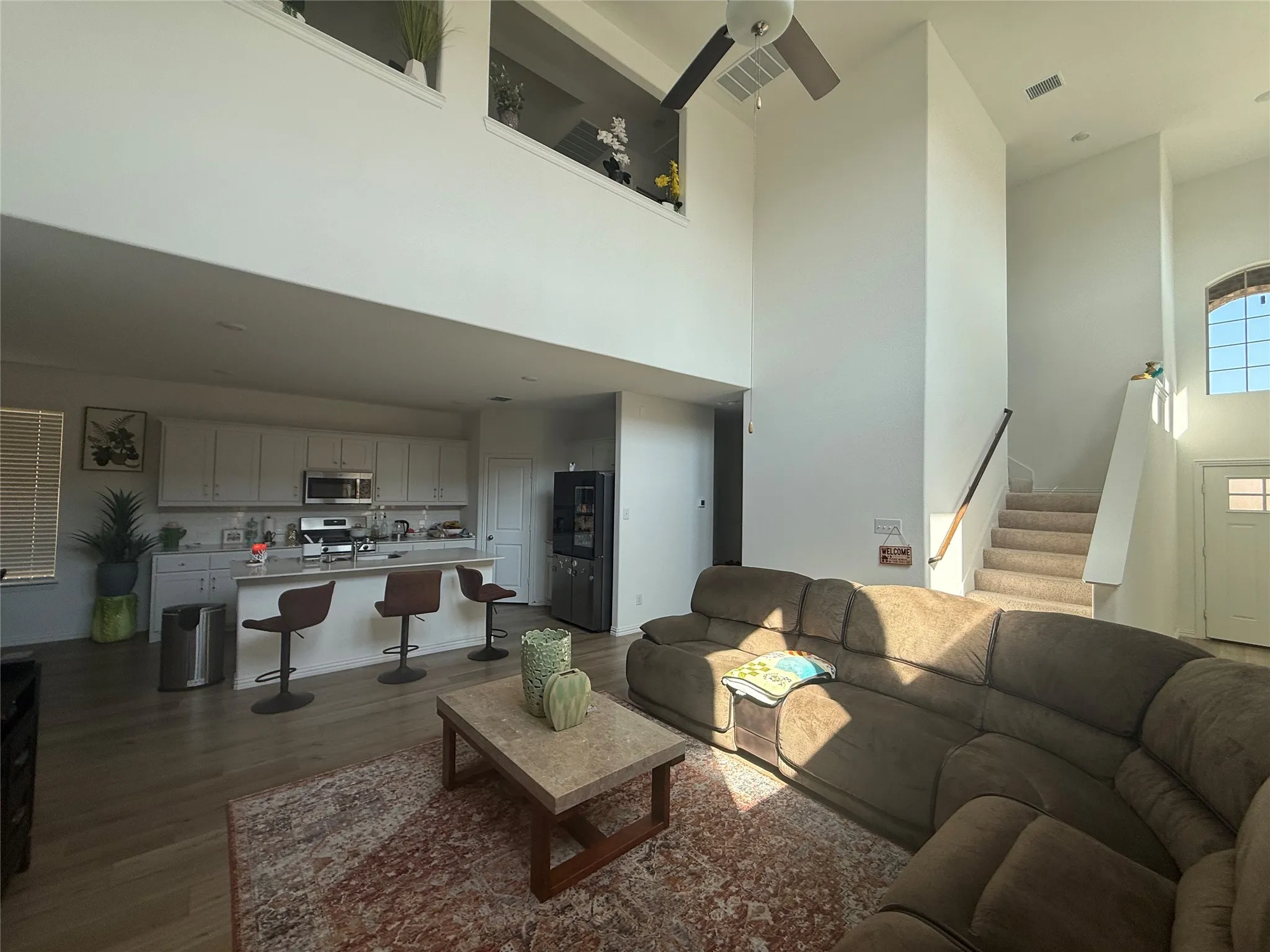 Open-concept living space featuring high ceilings, wood-finish flooring, and a kitchen with white cabinetry and a central island