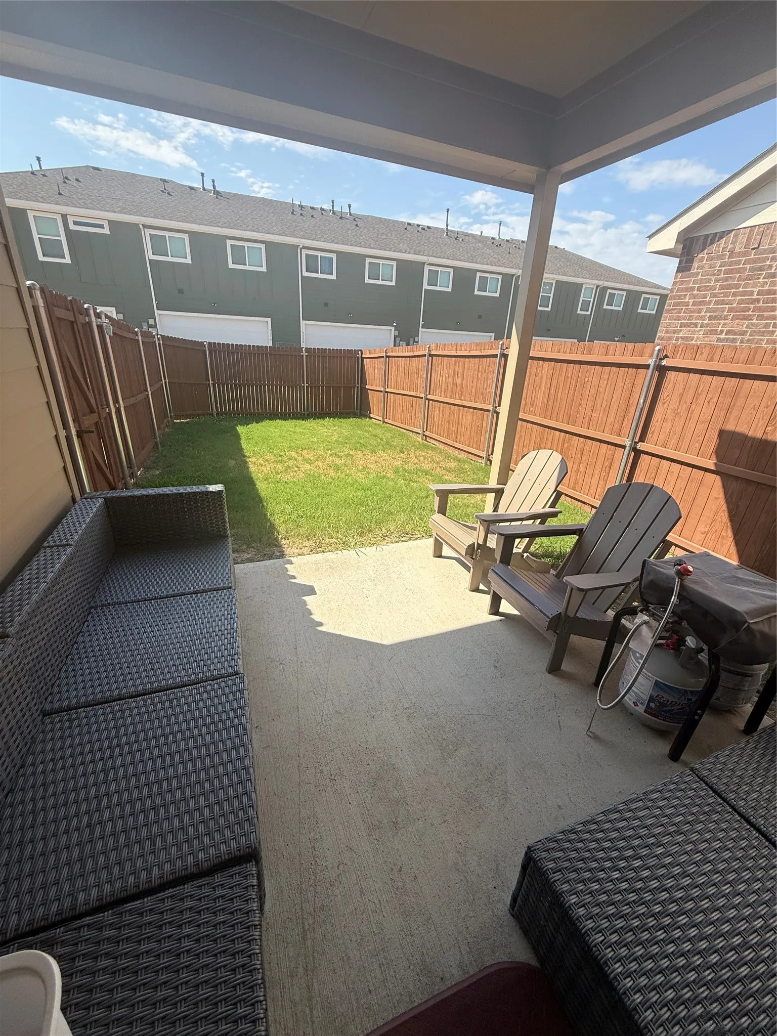 Covered concrete patio extending to a fenced backyard with a grass lawn