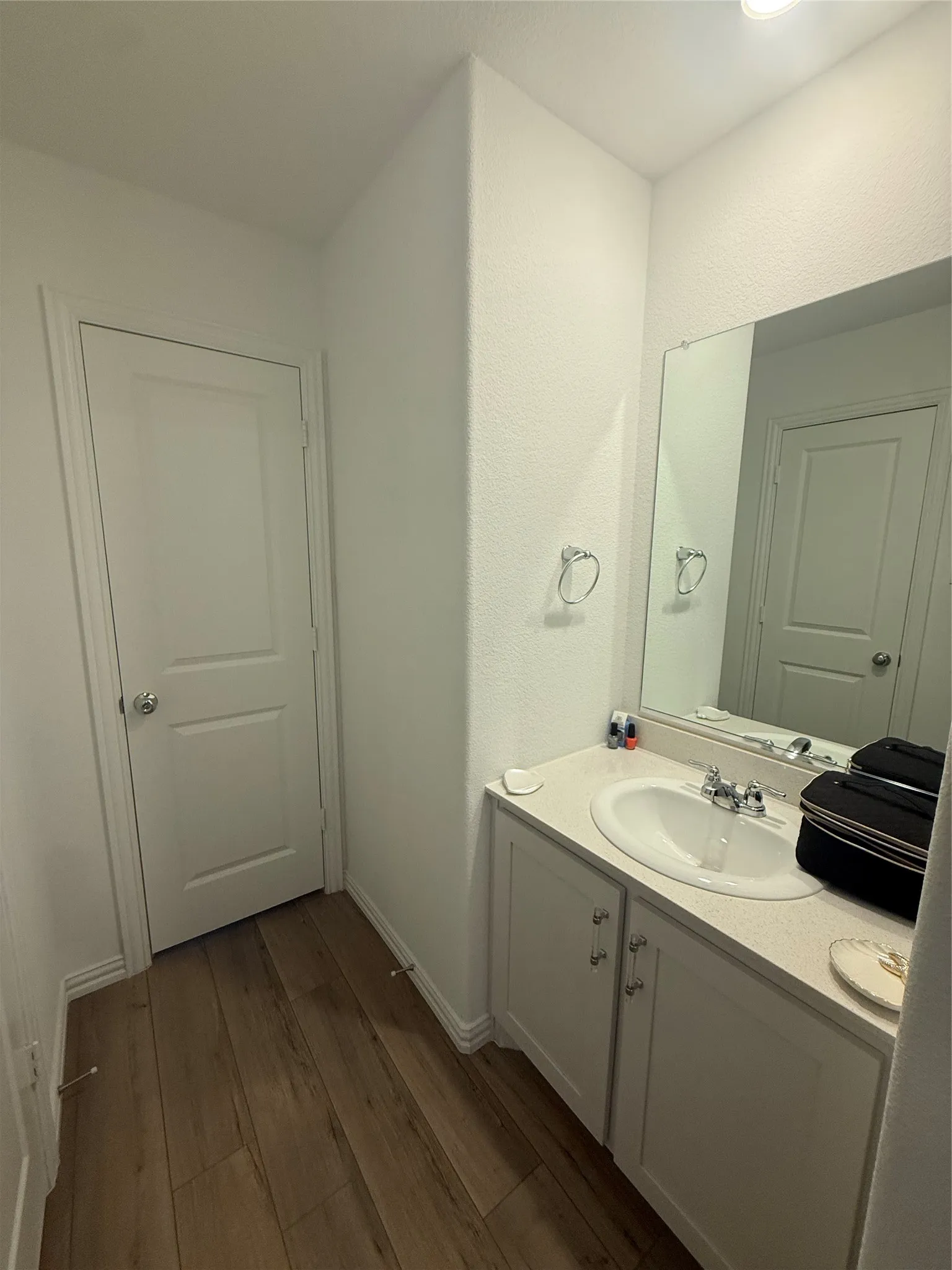 White vanity with an integrated sink and chrome faucet, set against wood-finish flooring