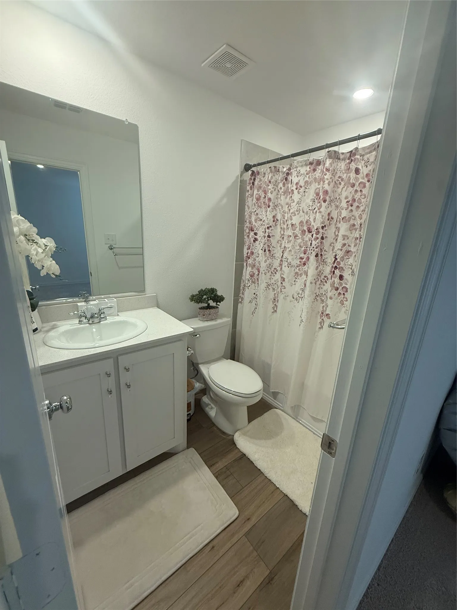Bathroom featuring a white vanity with an integrated sink, polished chrome faucet, wood-finish flooring, and recessed ceiling lighting