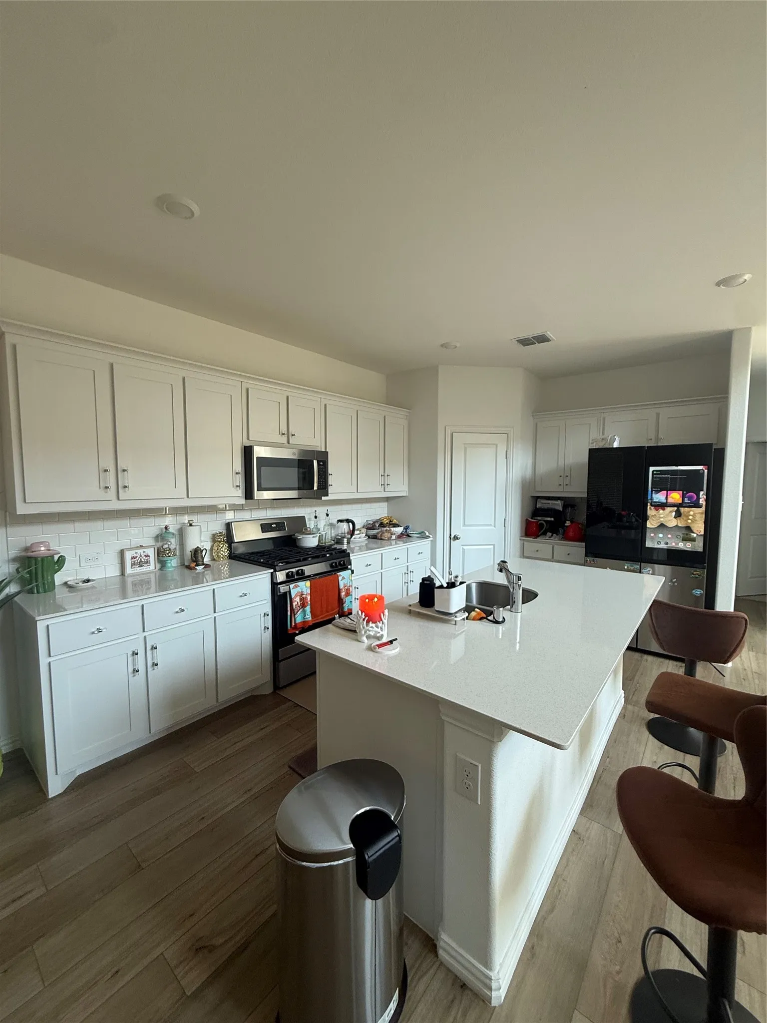 Modern kitchen featuring white shaker cabinetry, stainless steel appliances, a center island with an integrated sink, white countertops, and wood-finish flooring