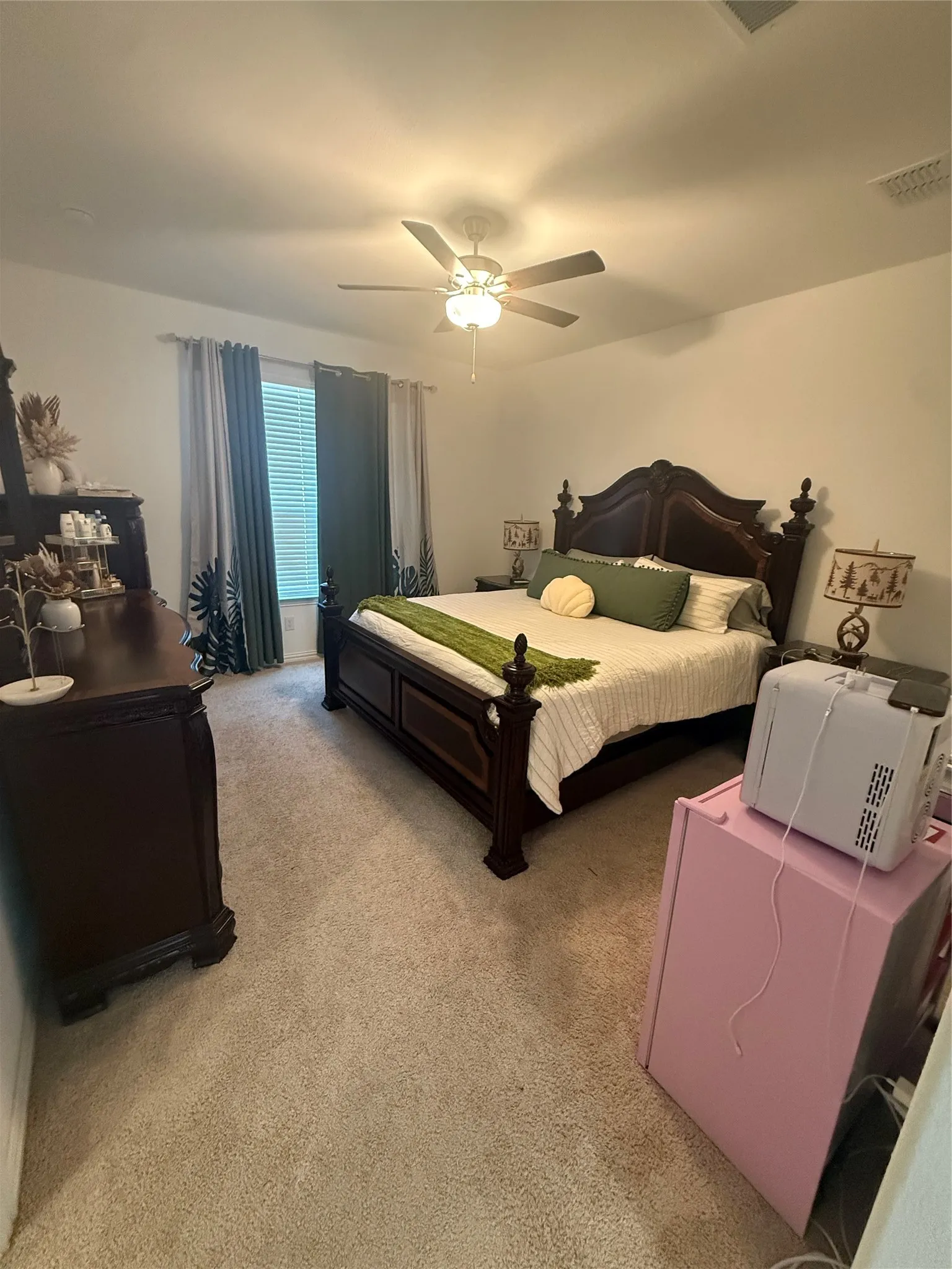 Carpeted bedroom with a ceiling fan light fixture and window with blinds and drapes