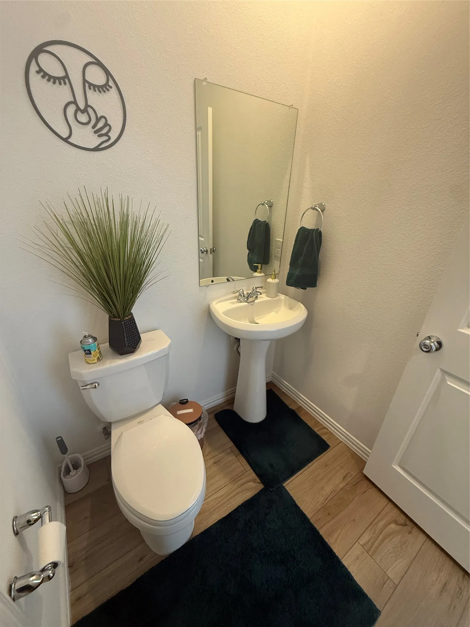 Pedestal sink with chrome-finish faucet, elongated toilet, and wood-finish flooring