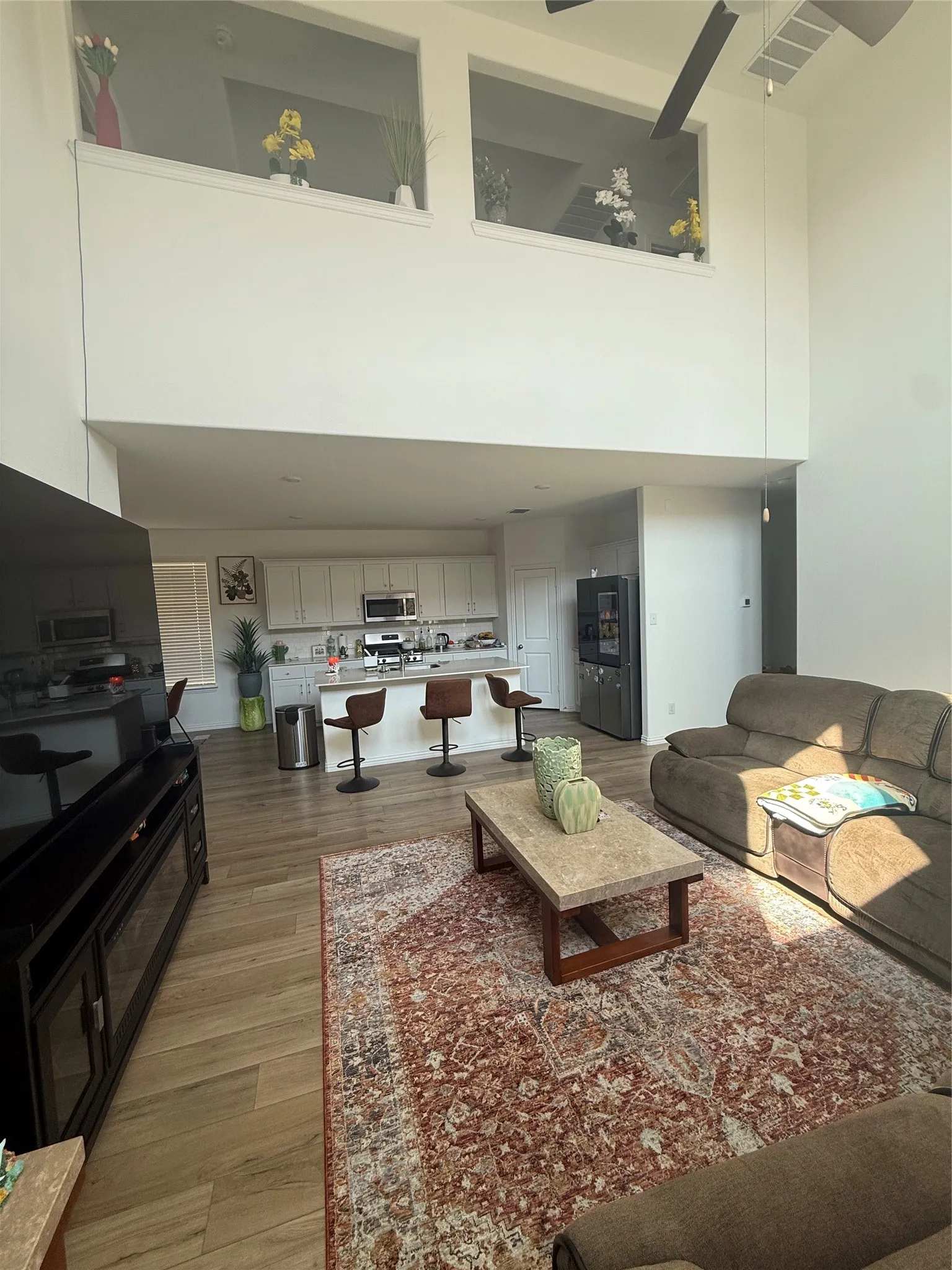 Open-concept living area featuring high ceilings, wood-finish flooring, and a kitchen with white cabinetry and a breakfast bar