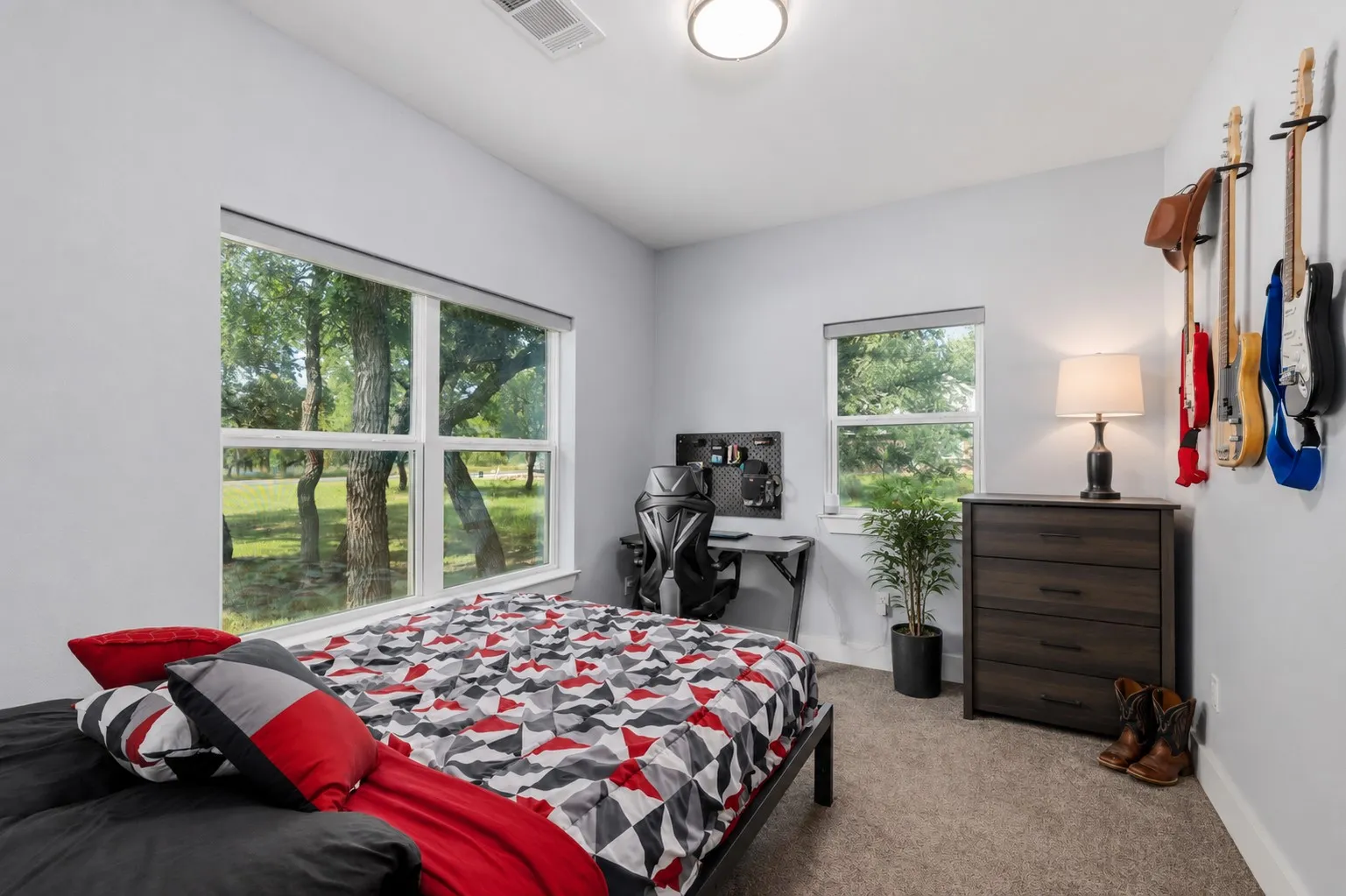 Carpeted room with light gray walls, featuring two windows with roller shades, a flush mount ceiling light, and a built-in air vent
