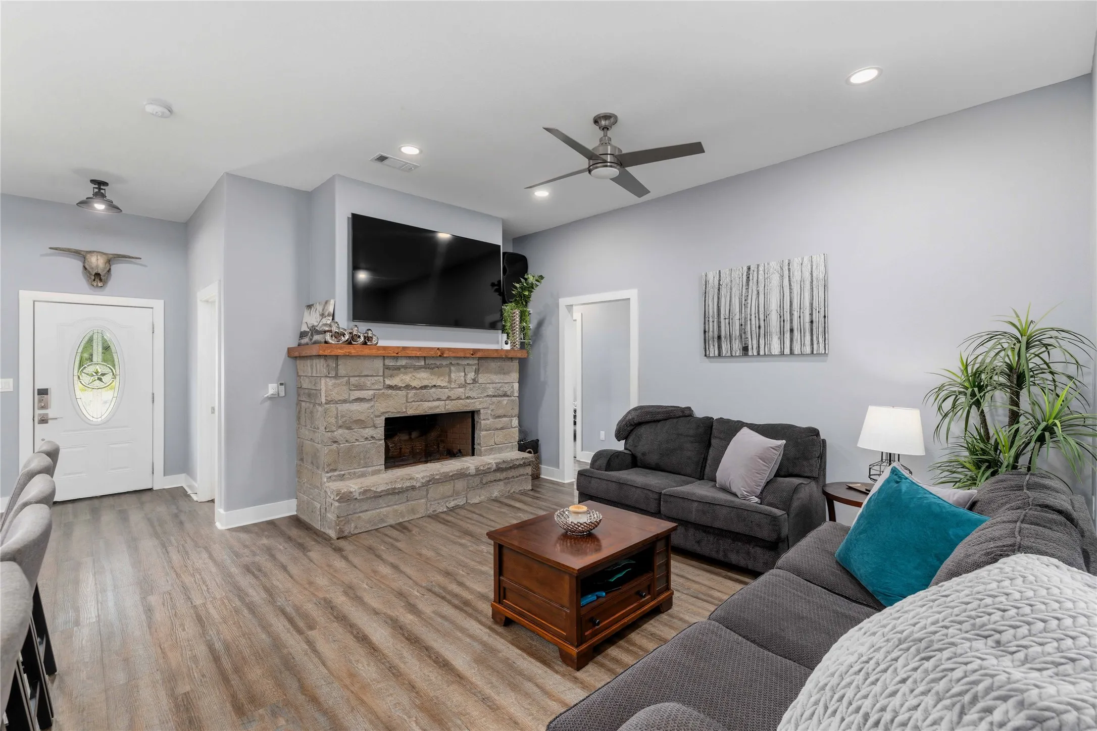 Living space featuring a stone fireplace with a wood mantle, wood-finish flooring, recessed lighting, and a ceiling fan