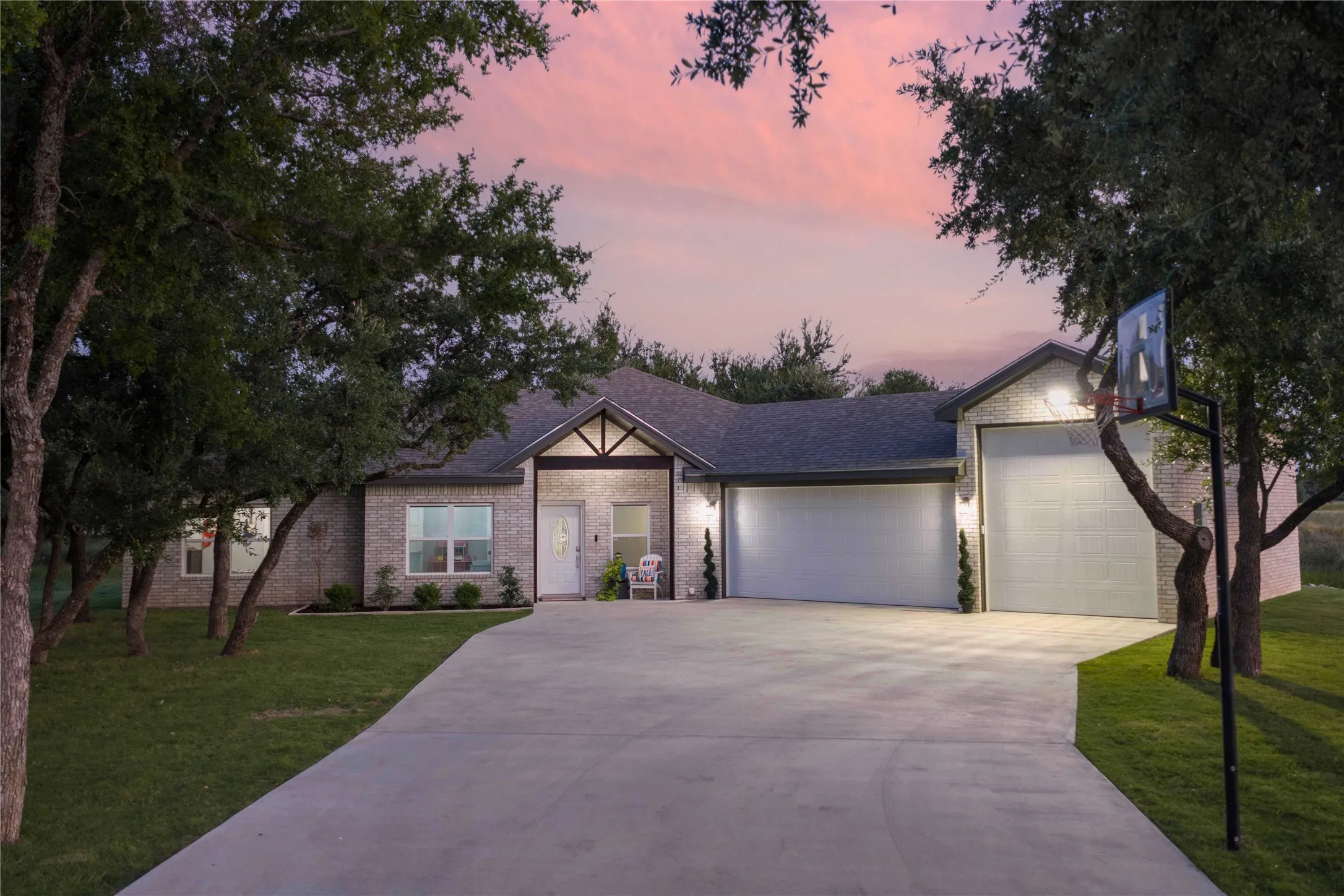 Brick facade residence featuring a concrete driveway, attached two-car garage, and mature trees