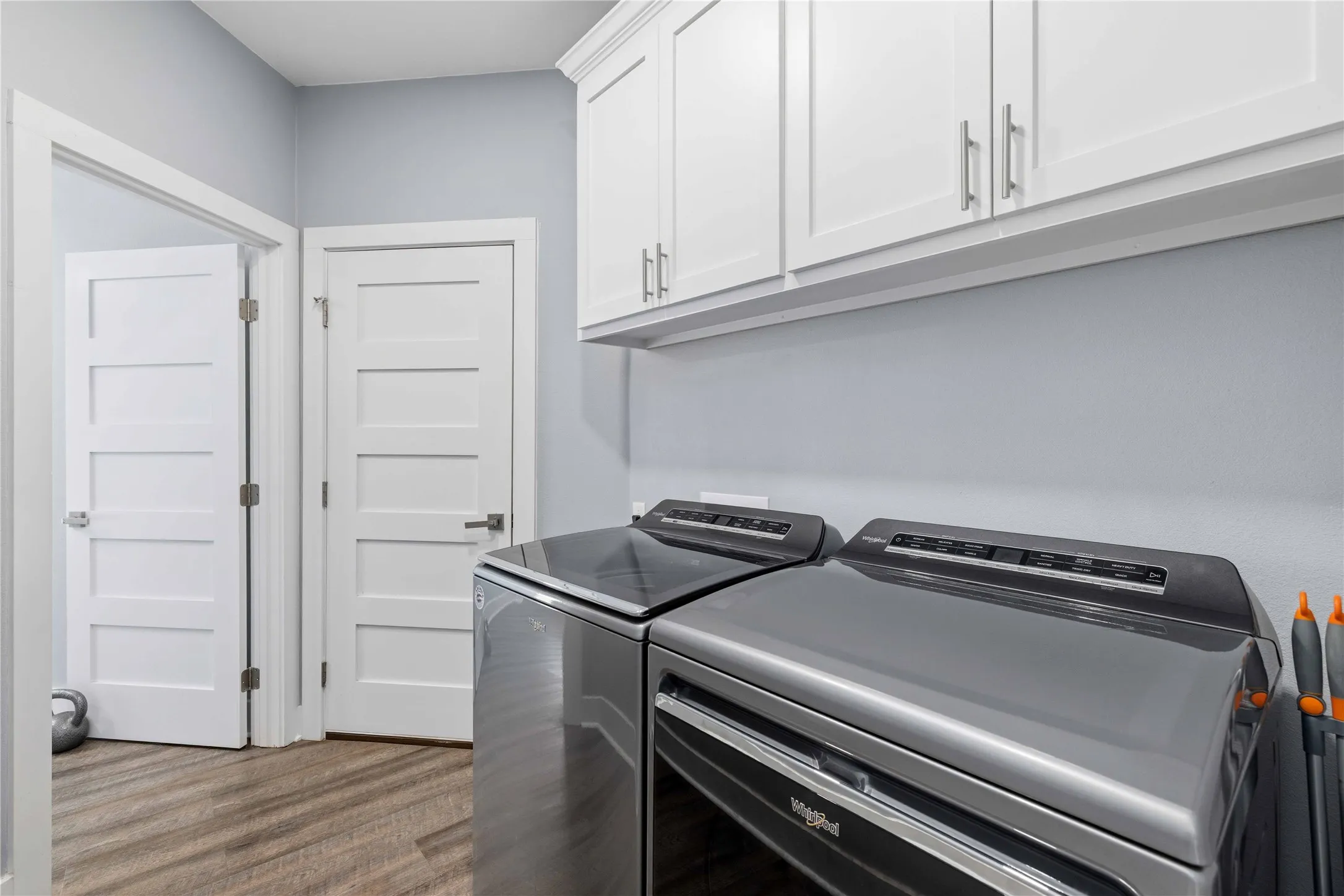 Laundry area featuring white shaker-style cabinetry with brushed nickel hardware, wood-finish flooring, and light gray wall paint