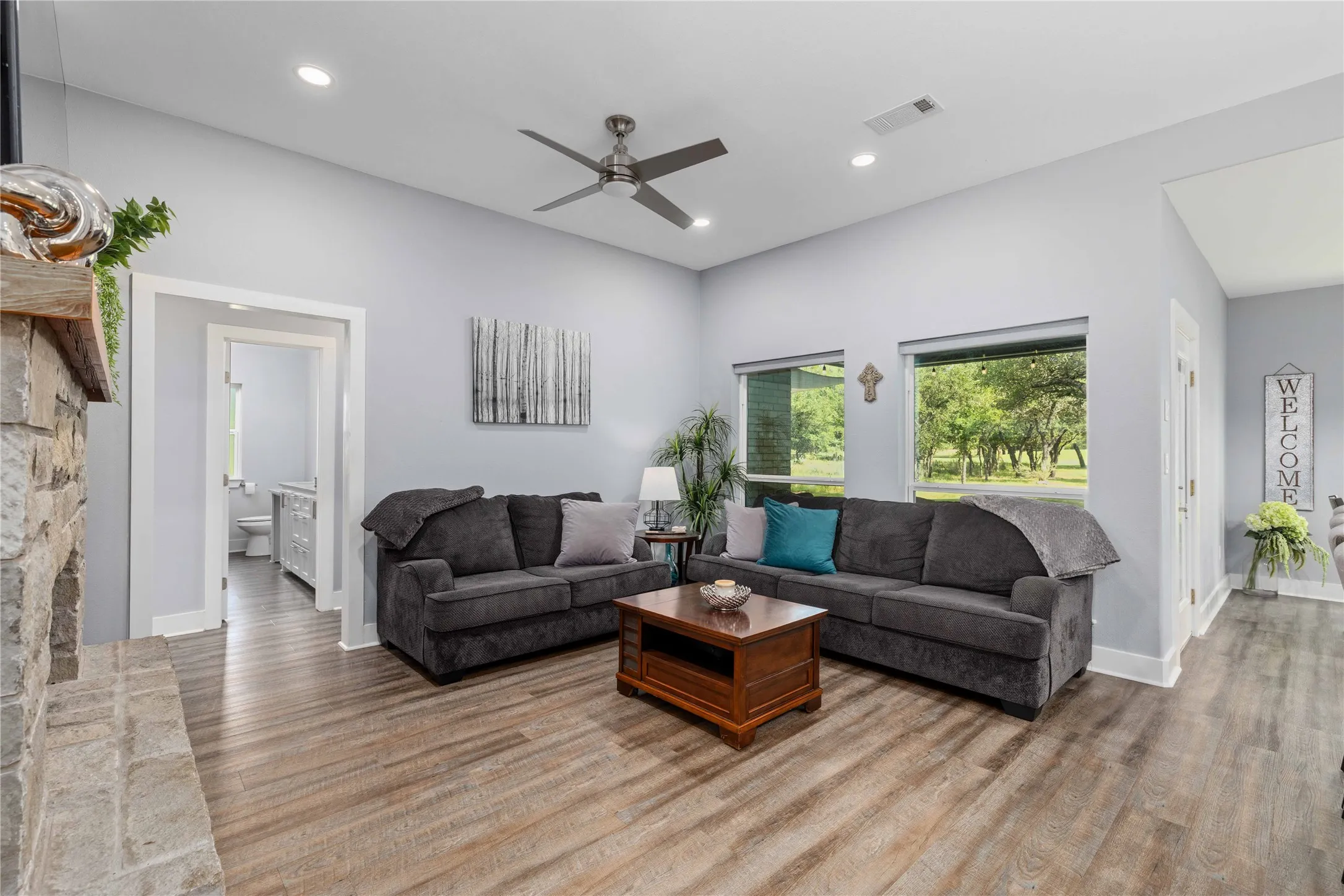 Spacious living area featuring wood-finish flooring, a stone fireplace, recessed lighting, and a ceiling fan