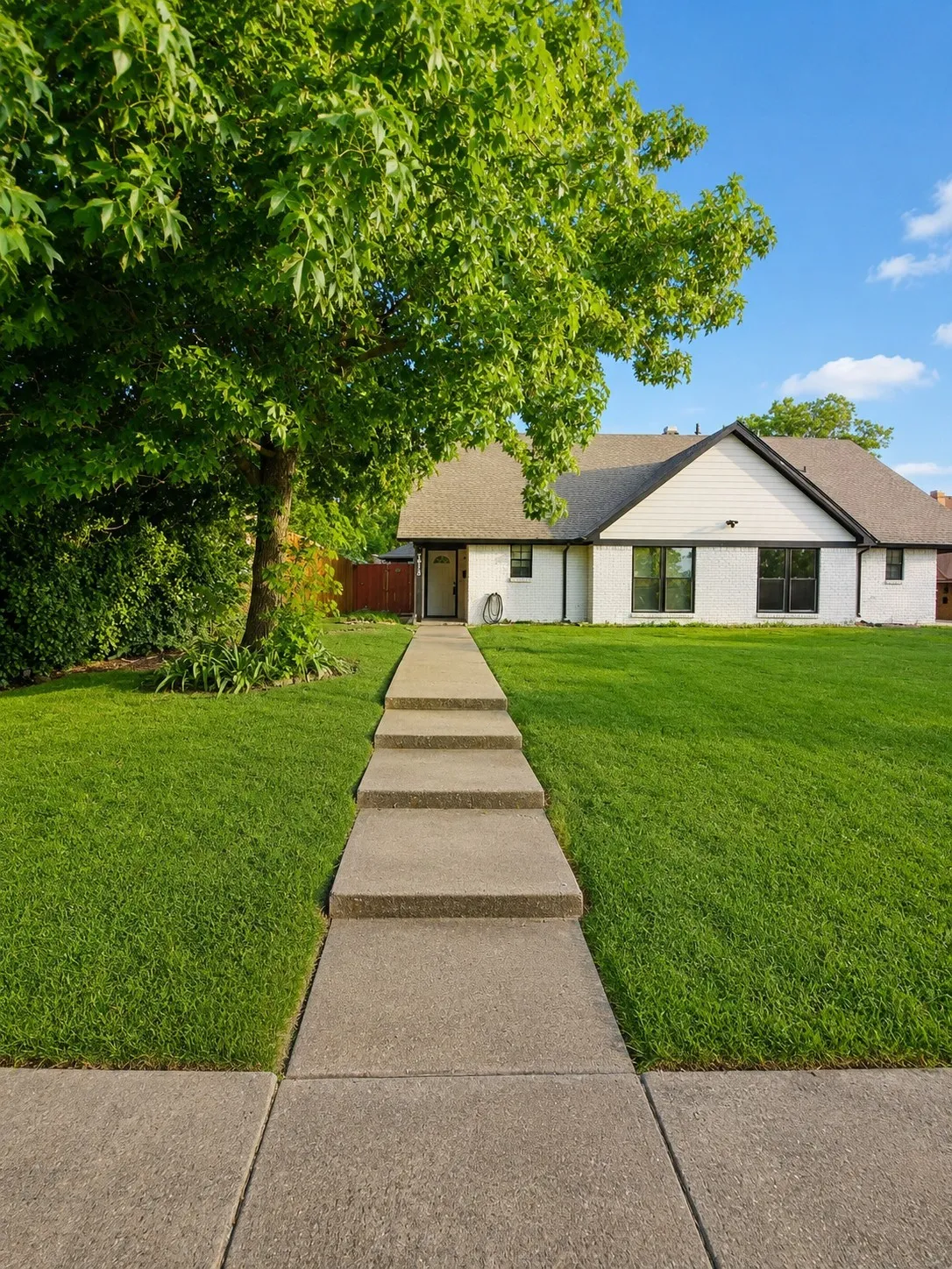 White brick exterior with dark trim accents, a front concrete walkway with integrated steps, and a lush green lawn