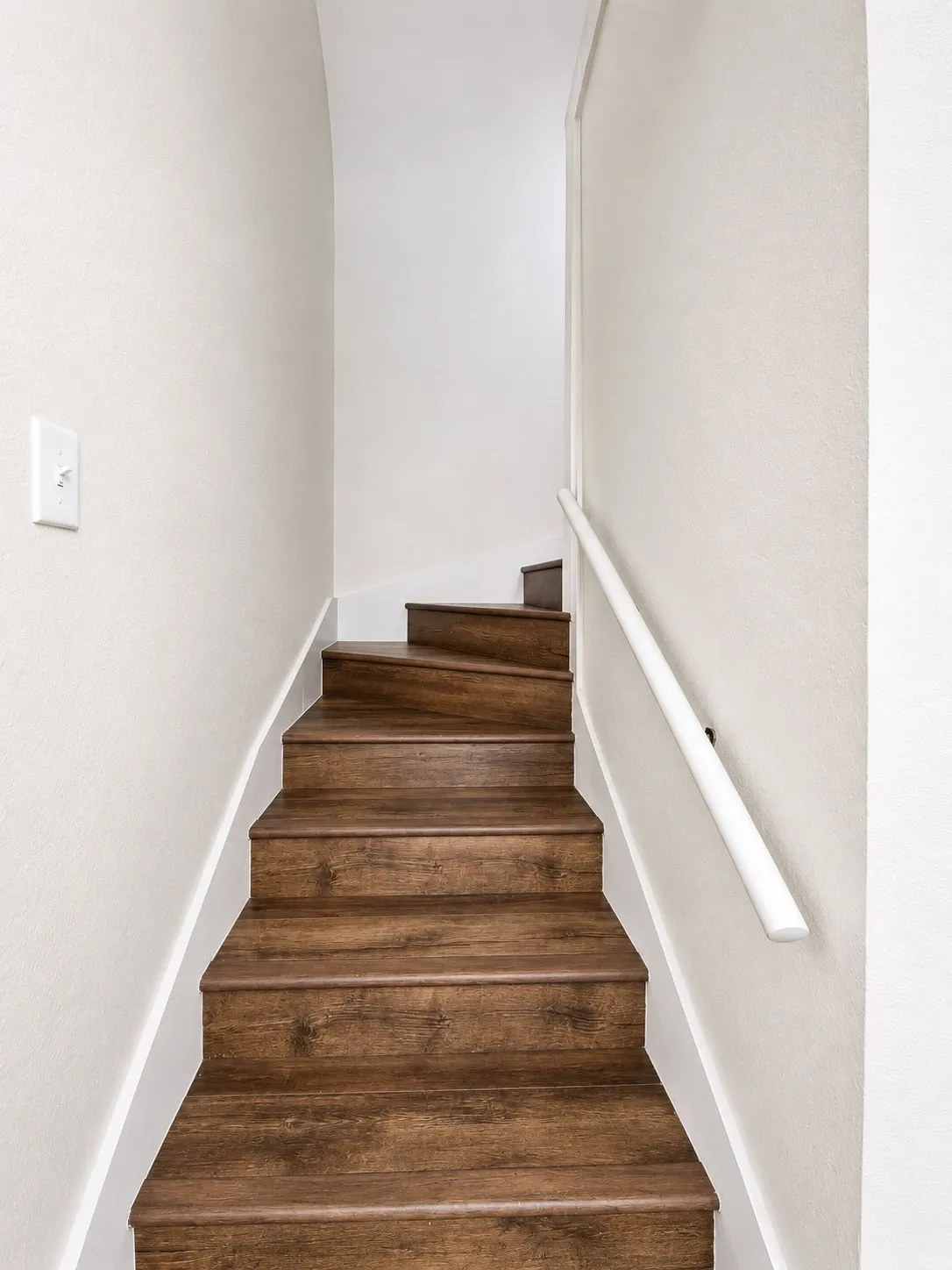 Staircase featuring wood-finish treads and risers, a white handrail, and light-toned walls