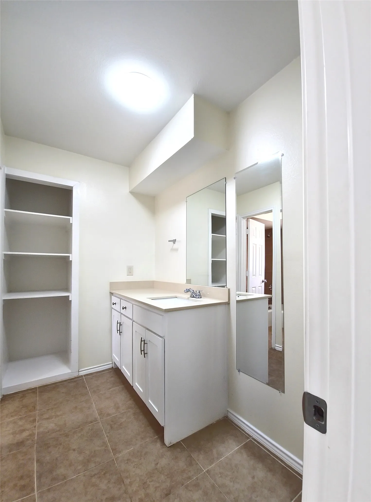 Bathroom featuring a dual-sink vanity with white cabinetry, built-in shelving, tile flooring, and mirror