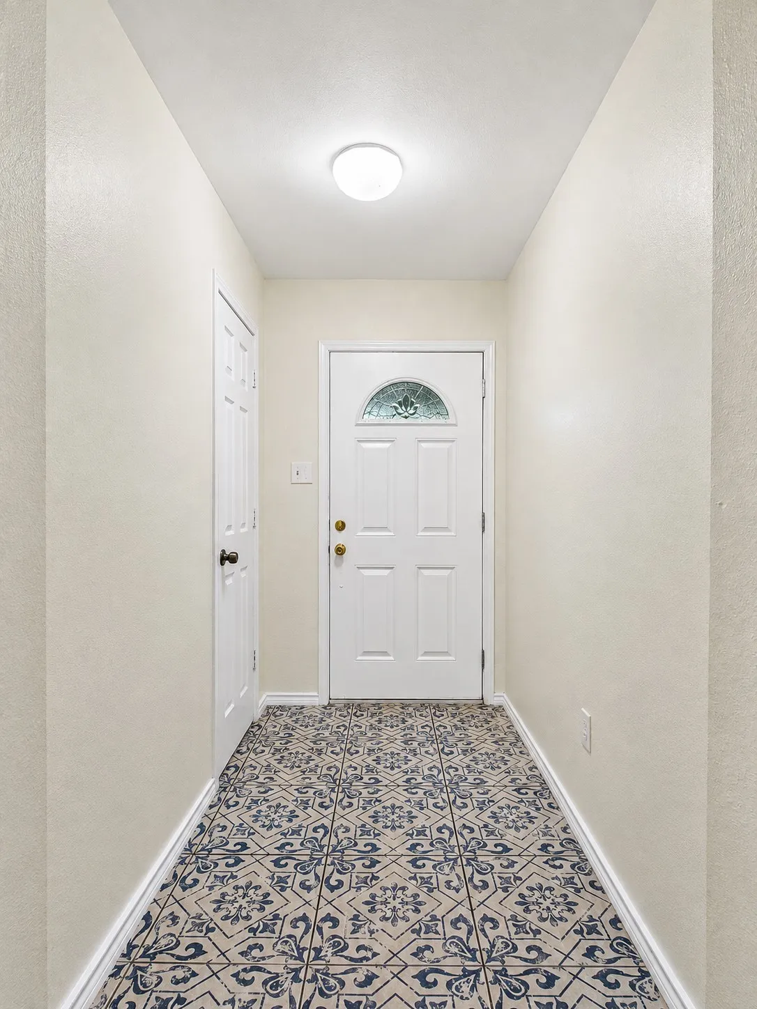 Entryway featuring patterned tile flooring, a white paneled door with decorative glass, and a flush-mount ceiling light